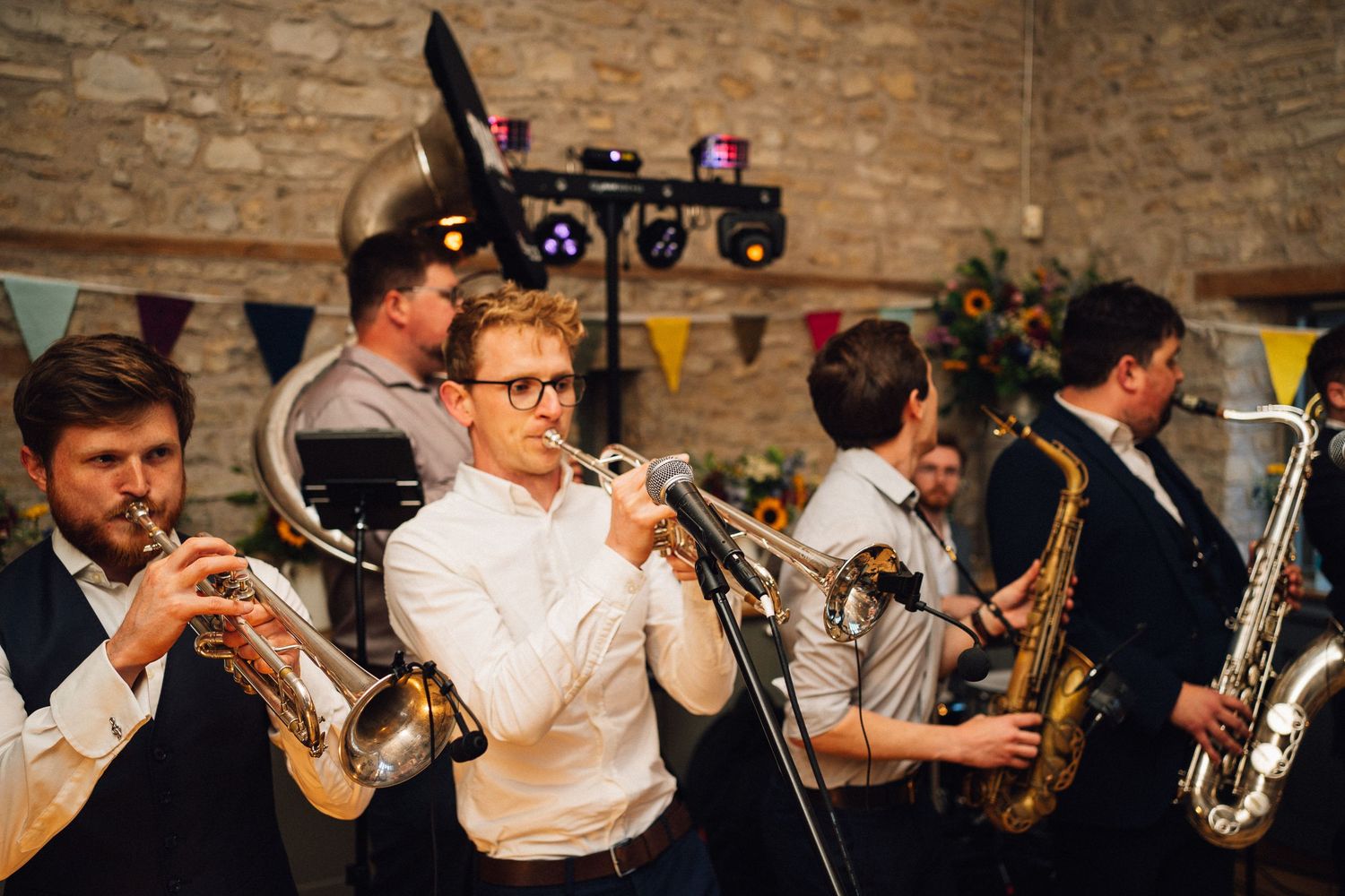 Musicians playing brass instruments during a wedding reception in a stone barn.