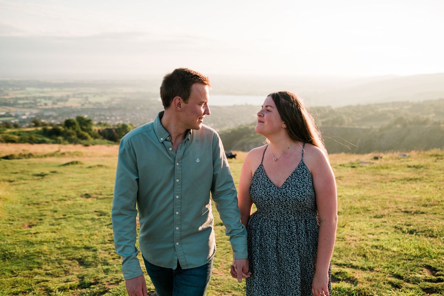 A couple enjoys a romantic moment on a hilltop meadow during golden hour sunset.