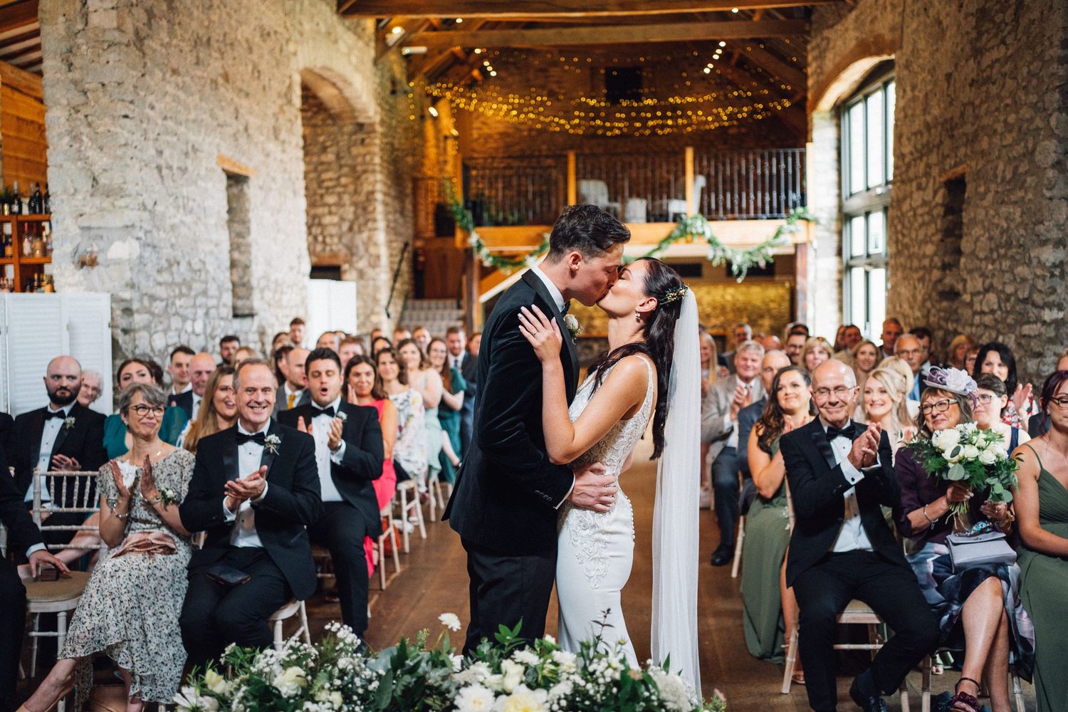 Wedding reception in a converted stone barn with twinkling lights and celebrating guests.