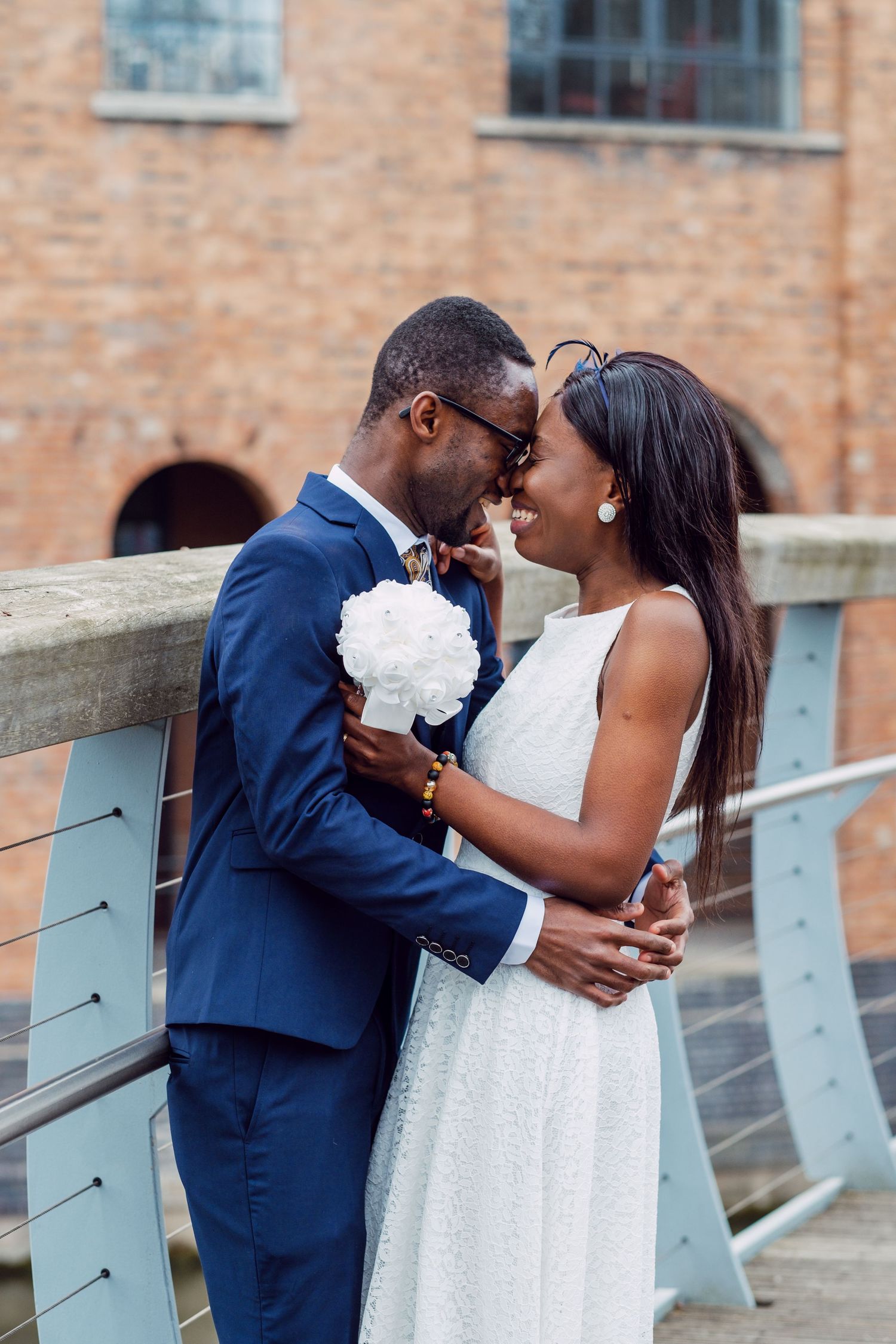 Intimate moment captured between couple on bridge with turquoise railings and brick architecture.