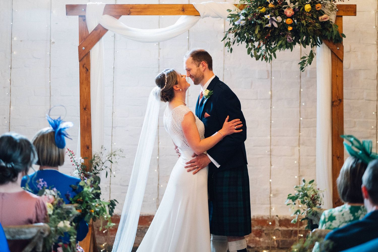 Wedding ceremony moment captured in a bright, airy barn with white walls and wooden beams.