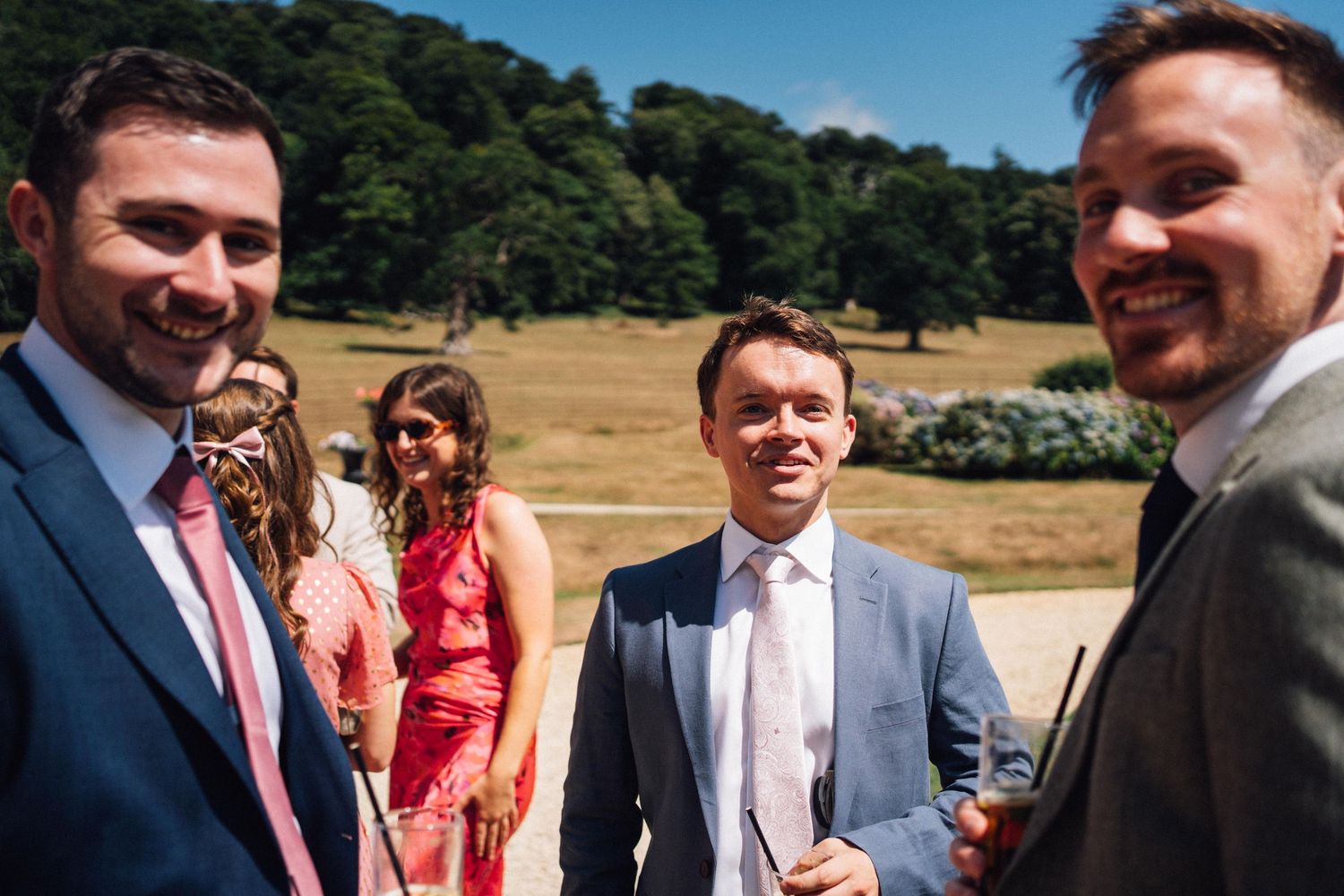 Wedding guests enjoying an outdoor celebration on a sunny day with trees in the background.