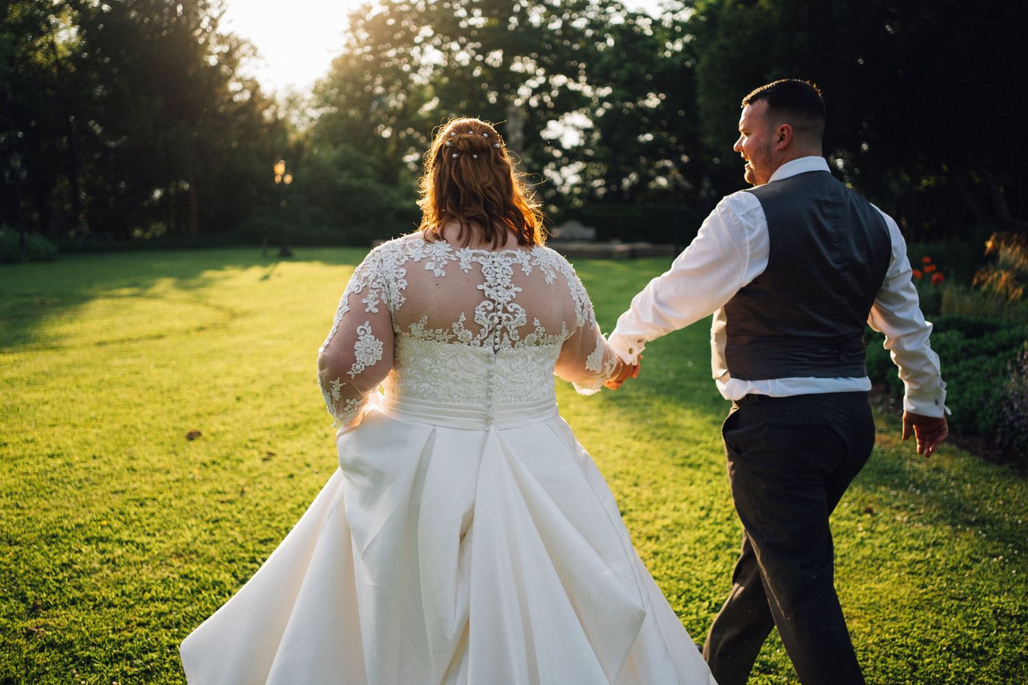 Newlywed couple walks hand in hand through a sunlit garden during golden hour wedding photography session.