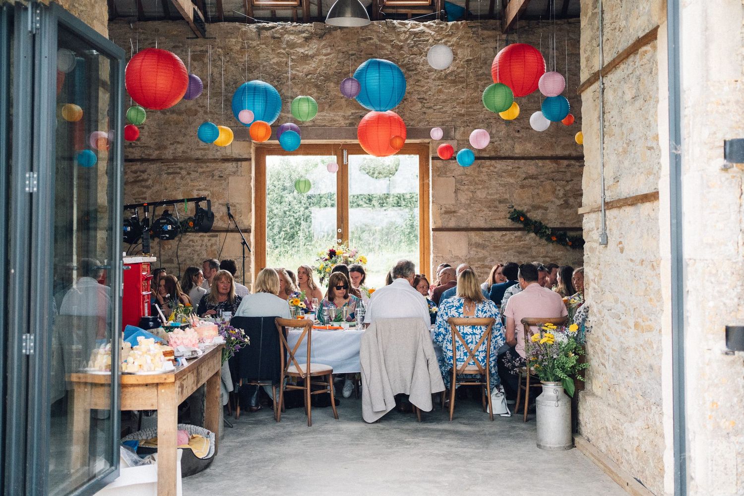 Interior of rustic barn venue decorated with colorful hanging paper lanterns for a celebration.