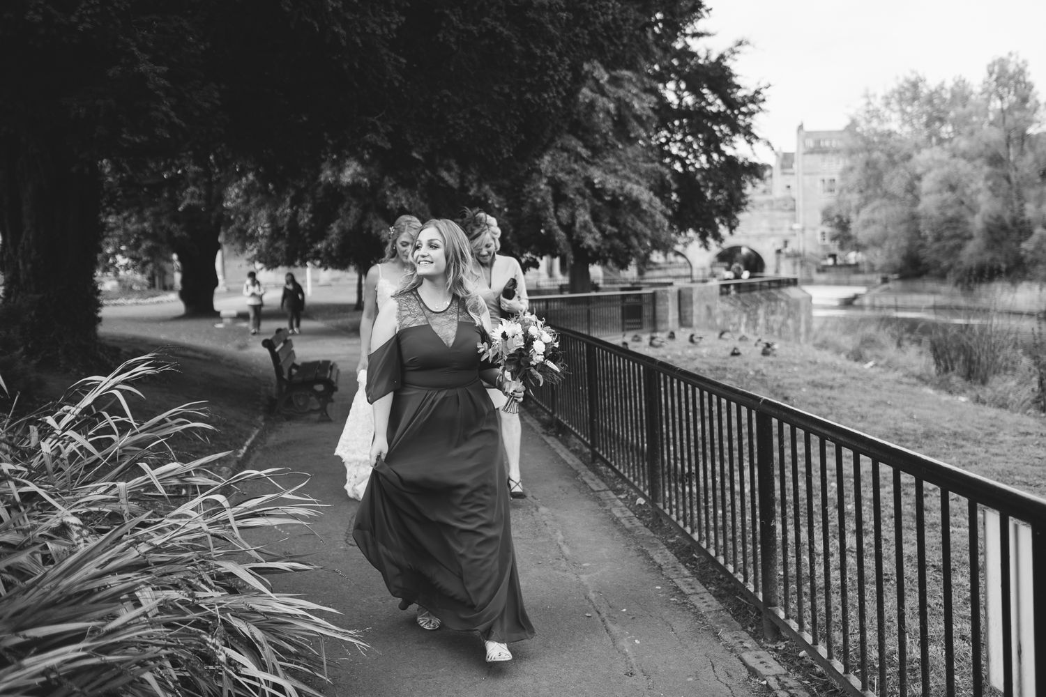 People stroll along a scenic pathway bordered by an iron railing and trees.