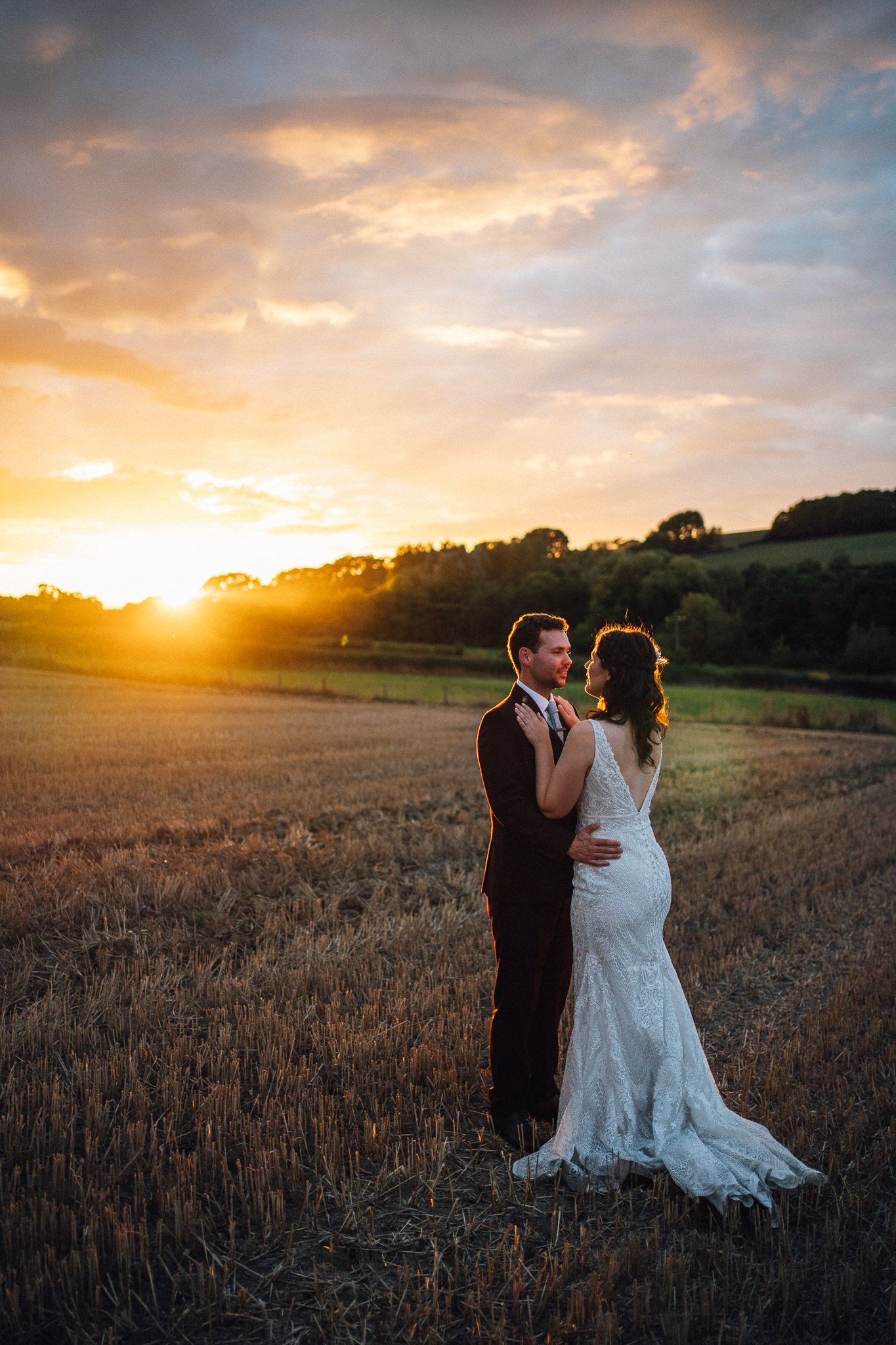 A couple embraces in a wheat field during a golden sunset on their wedding day.