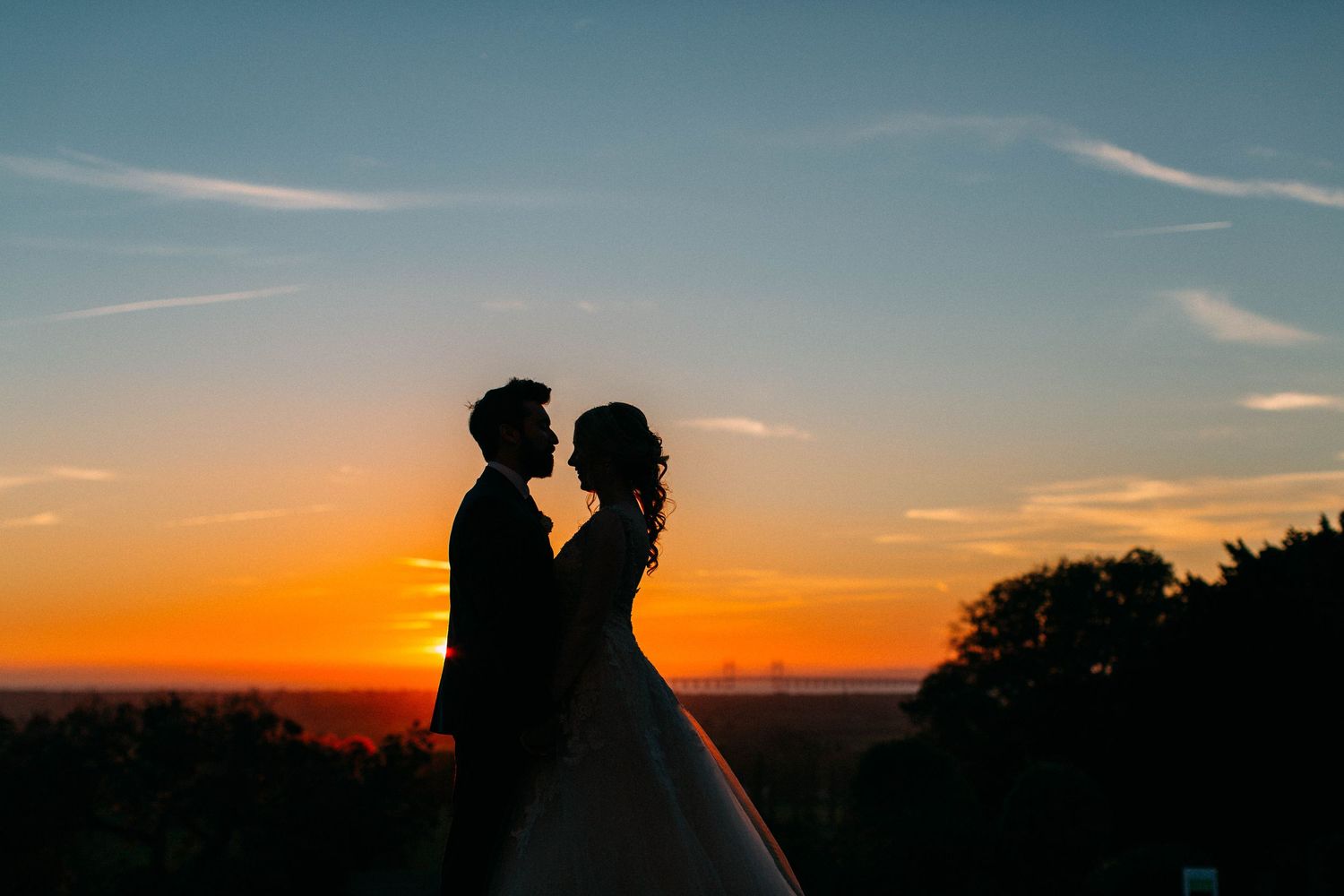 Silhouettes of figures stand against a vibrant orange and blue sunset sky on the horizon.