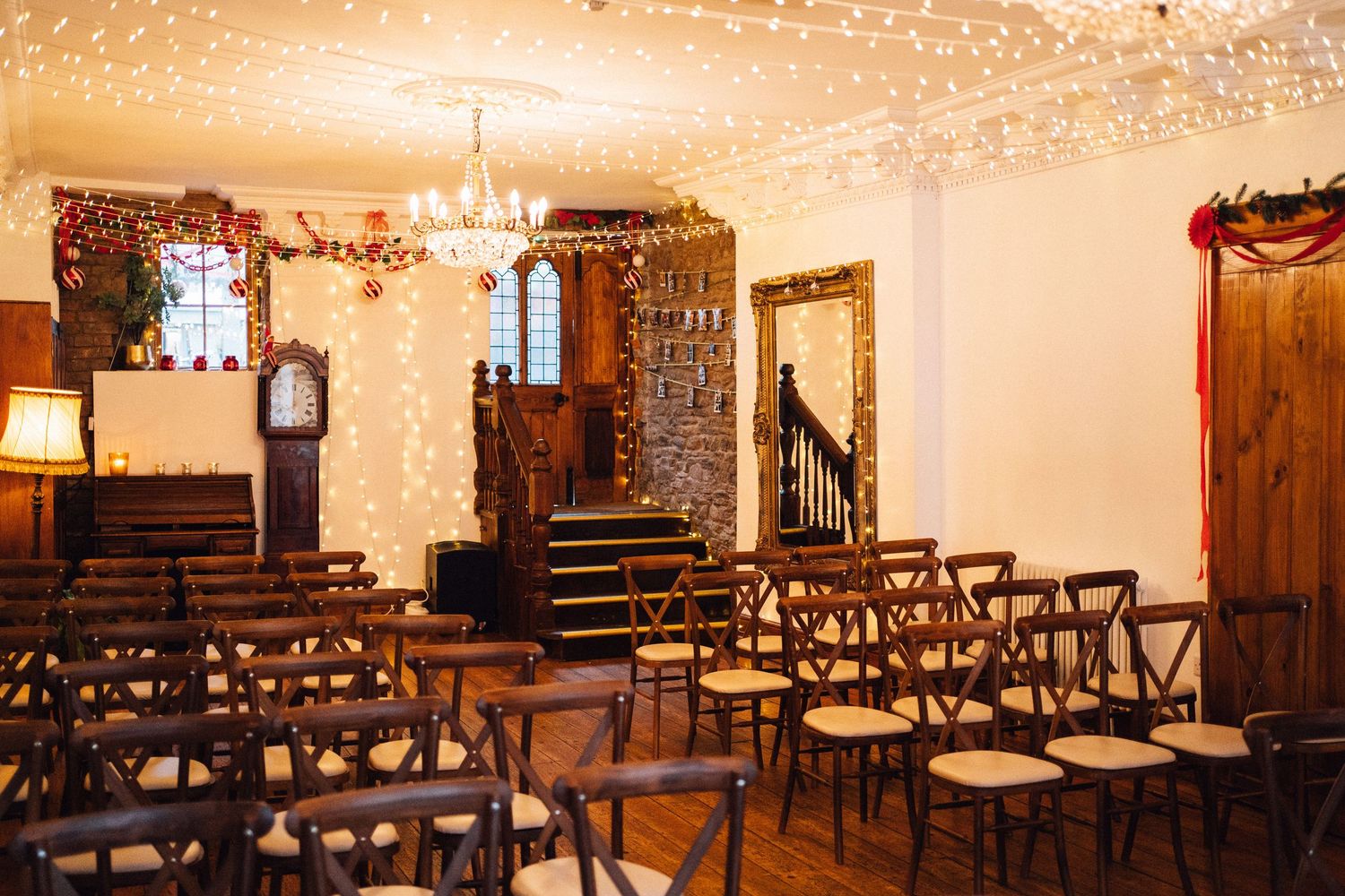 Elegant wedding venue interior with wooden chairs arranged in rows and ornate chandeliers casting warm light.