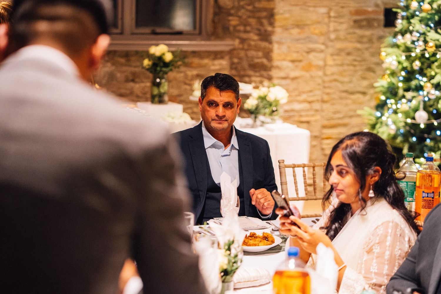 Wedding guests enjoying a reception dinner in a rustic barn venue with exposed brick walls and string lights.