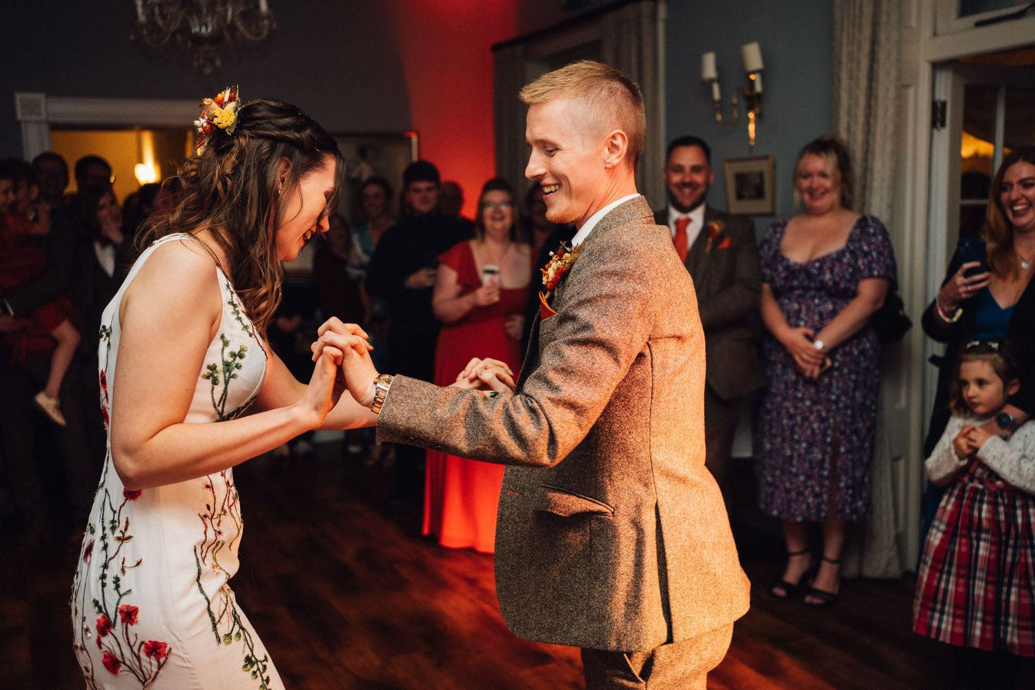 Wedding guests dancing and celebrating on a dimly lit dance floor with red ambient lighting.