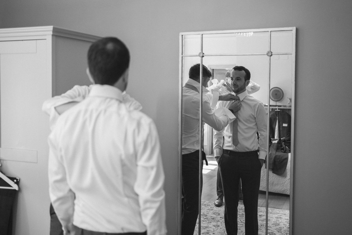 A series of black and white photographs showing someone adjusting their tie and getting dressed in formal attire.