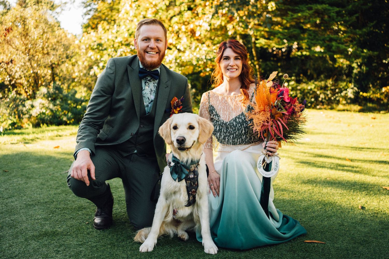 A couple and their happy golden retriever enjoy outdoor wedding photos in golden sunlight.