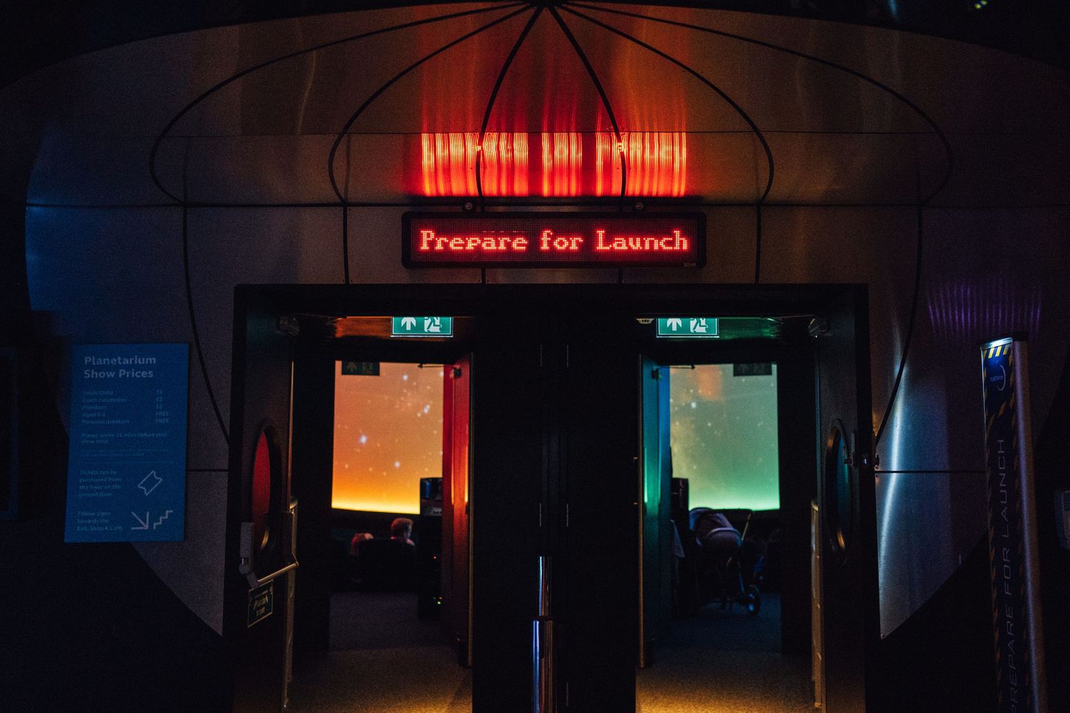 Dramatic dark entrance with neon 'Prepare for Launch' sign and glowing doors at a space-themed attraction.