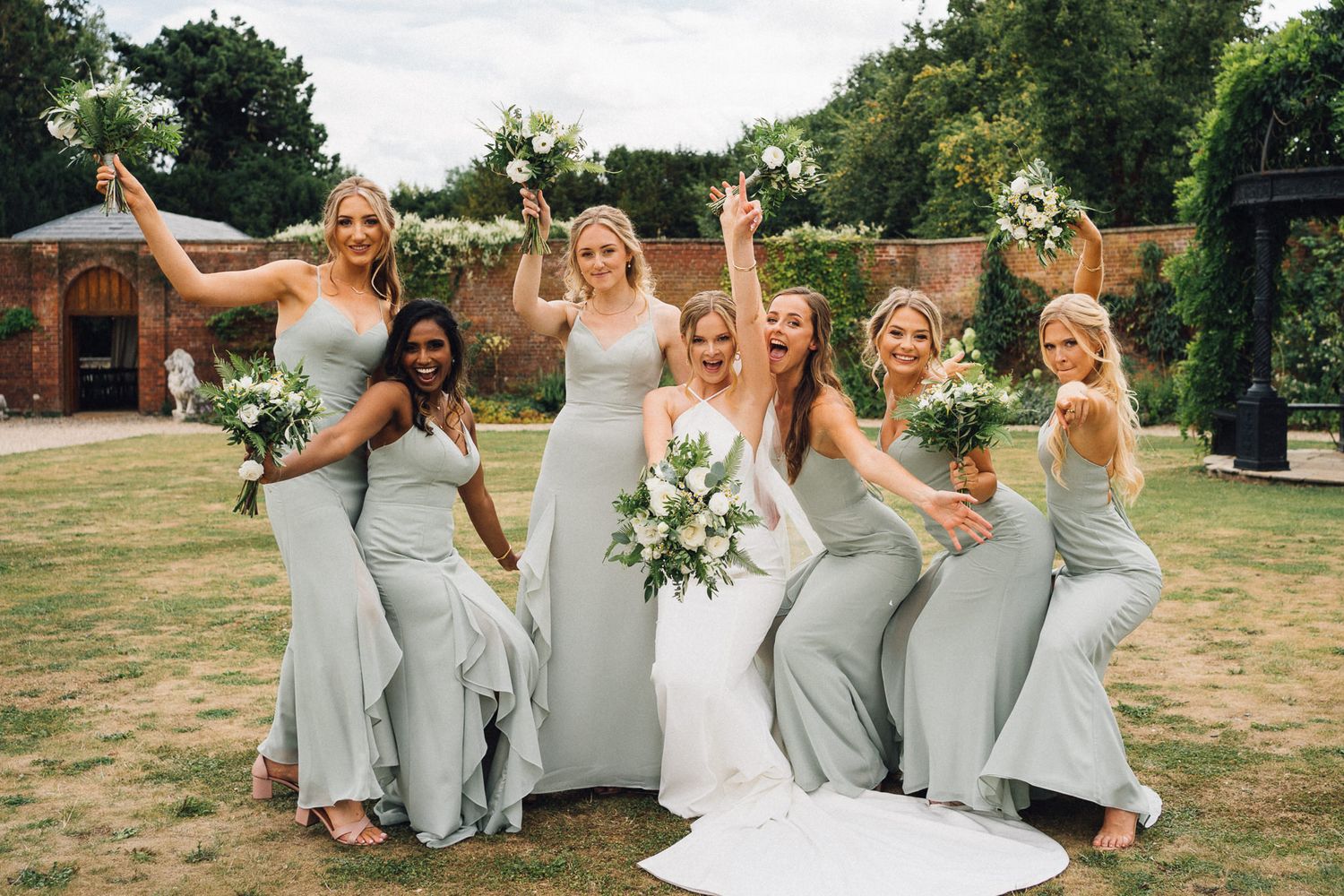 Bridal party in gray dresses celebrating joyfully during outdoor photo session.