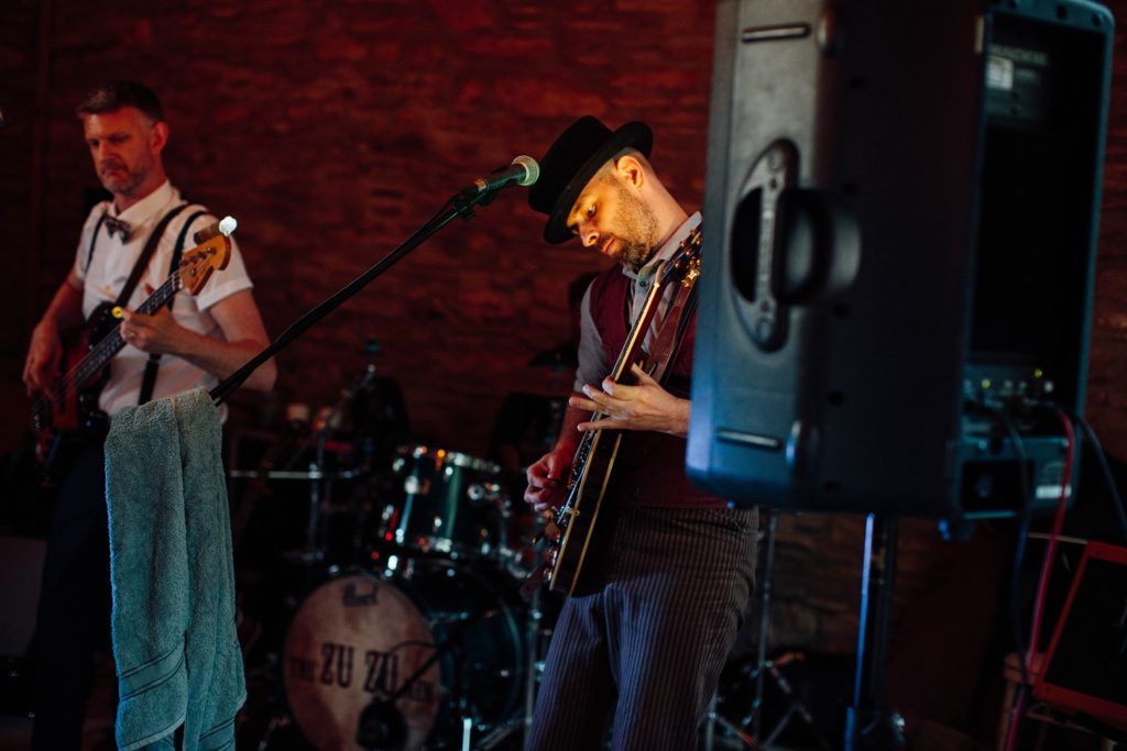 Band performs on stage in a dimly lit brick-walled venue with musical instruments.