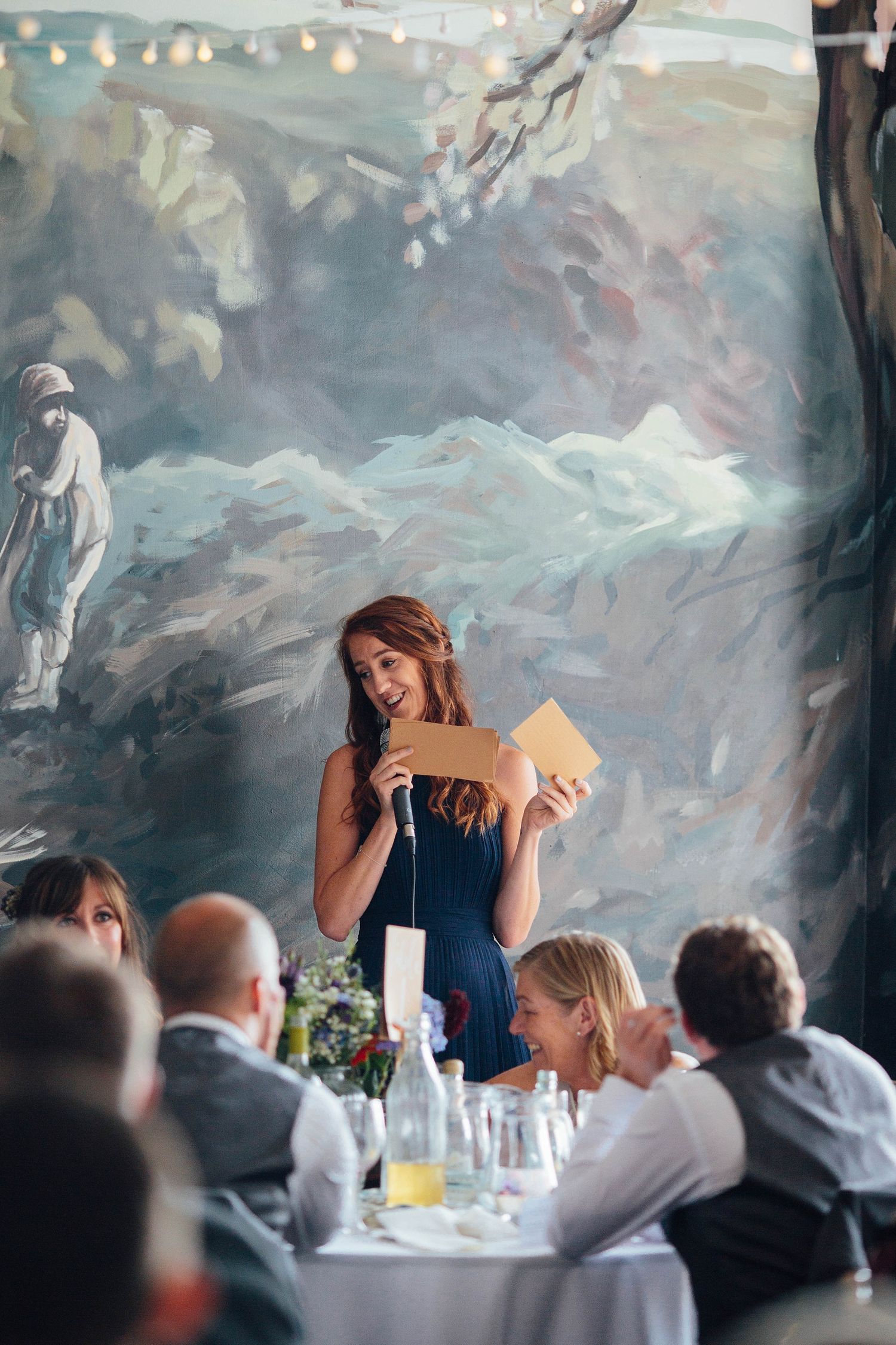 A woman in a navy dress delivers a heartfelt speech at an elegant wedding reception.