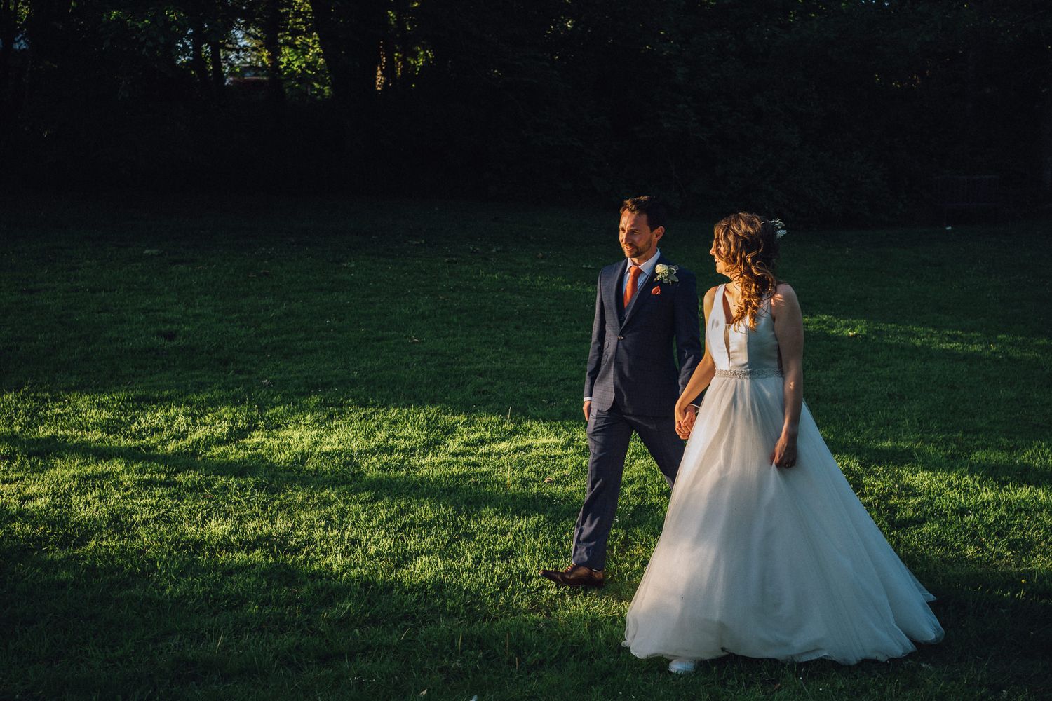 Couple walking across a sunlit lawn during golden hour at their wedding celebration.
