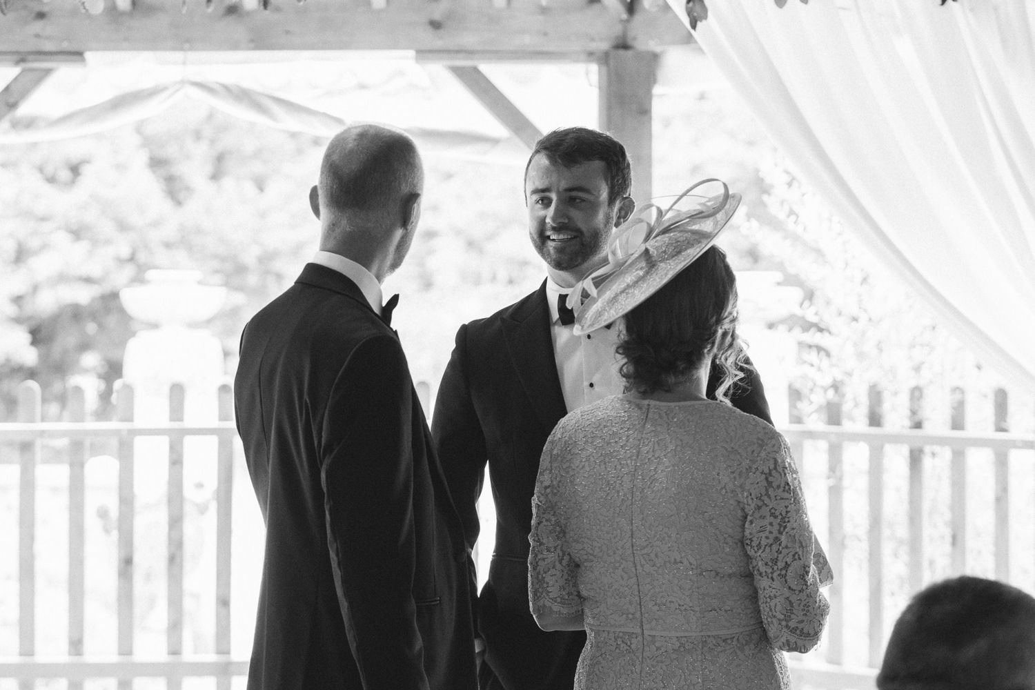 Wedding party members gather in a rustic barn space with exposed wooden beams and white draping.