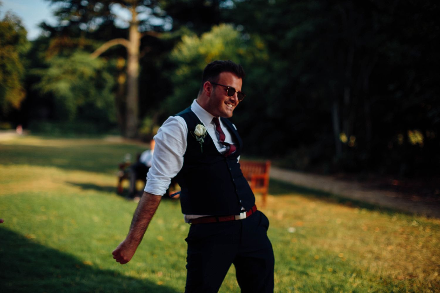 Person in vest and dress shirt dancing energetically on grass at sunset.