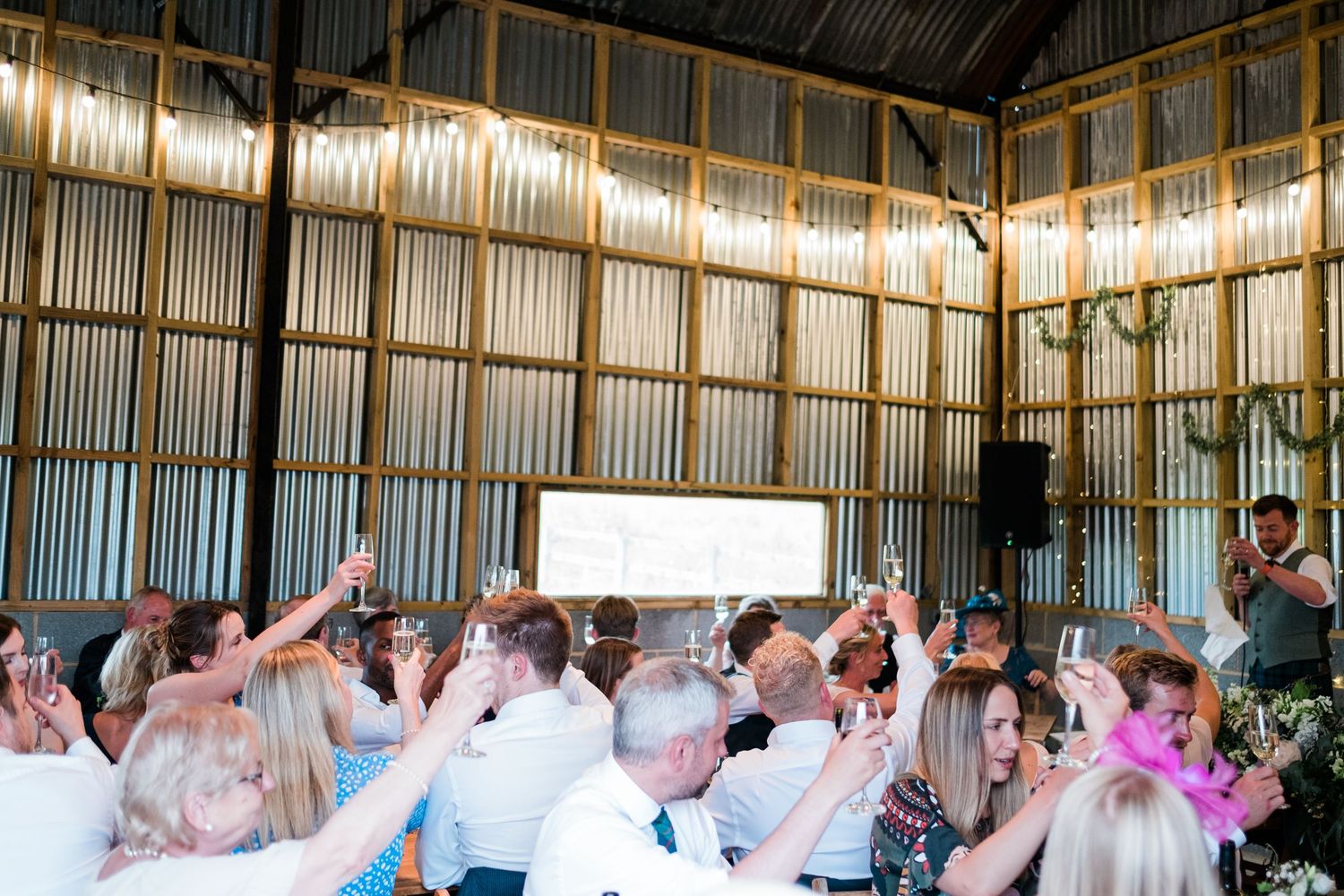 Celebration crowd with raised hands inside a barn venue with string lights and metal walls.