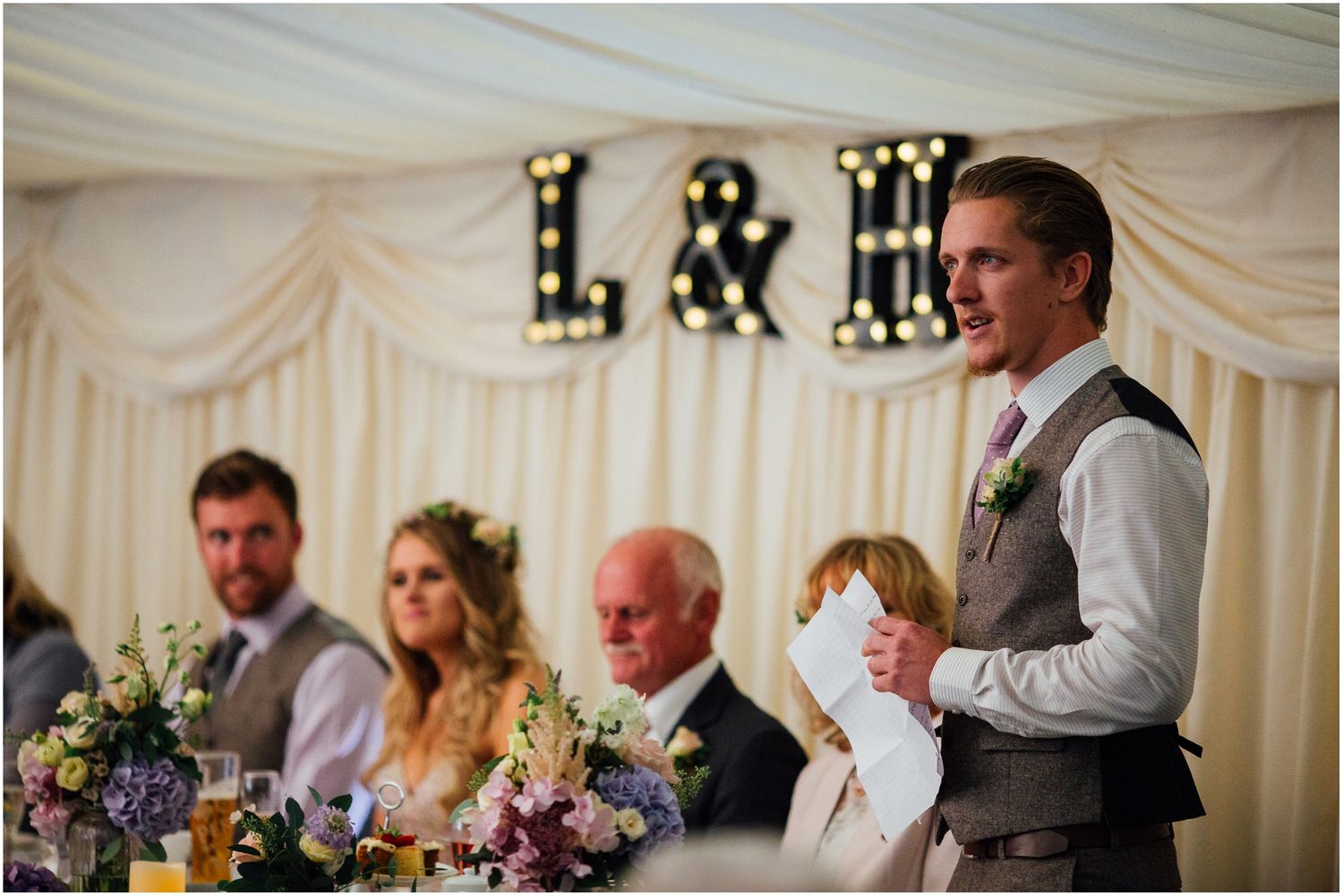 Wedding reception setup with illuminated letters and white draping in an elegant marquee.