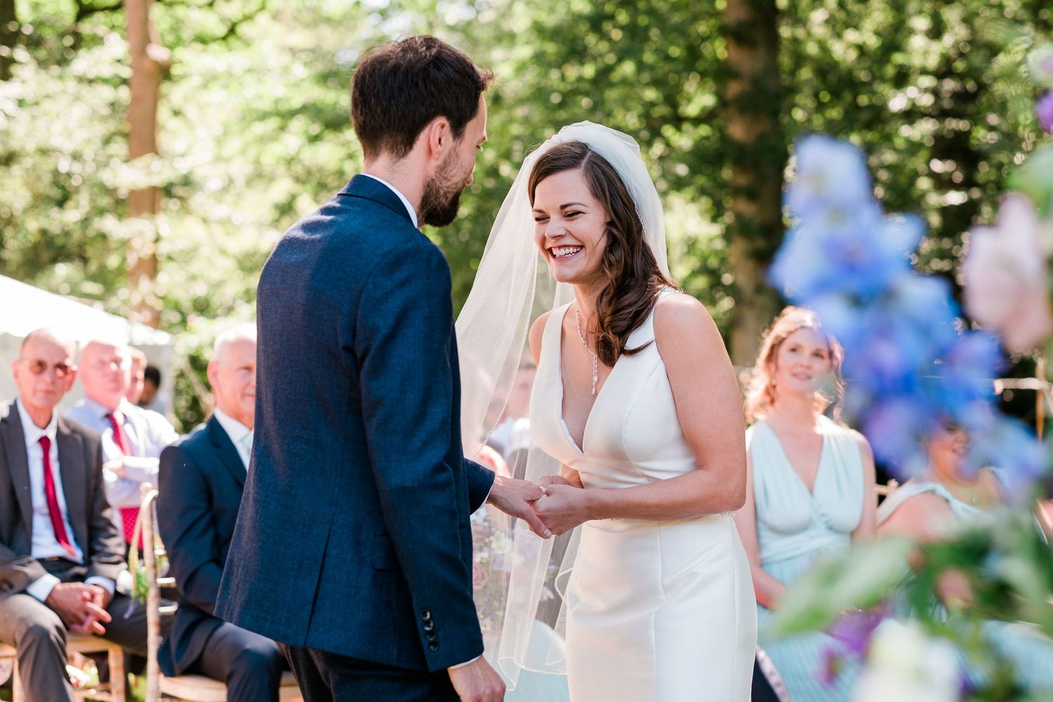Sunlit outdoor wedding ceremony with blue and floral accents among the trees.
