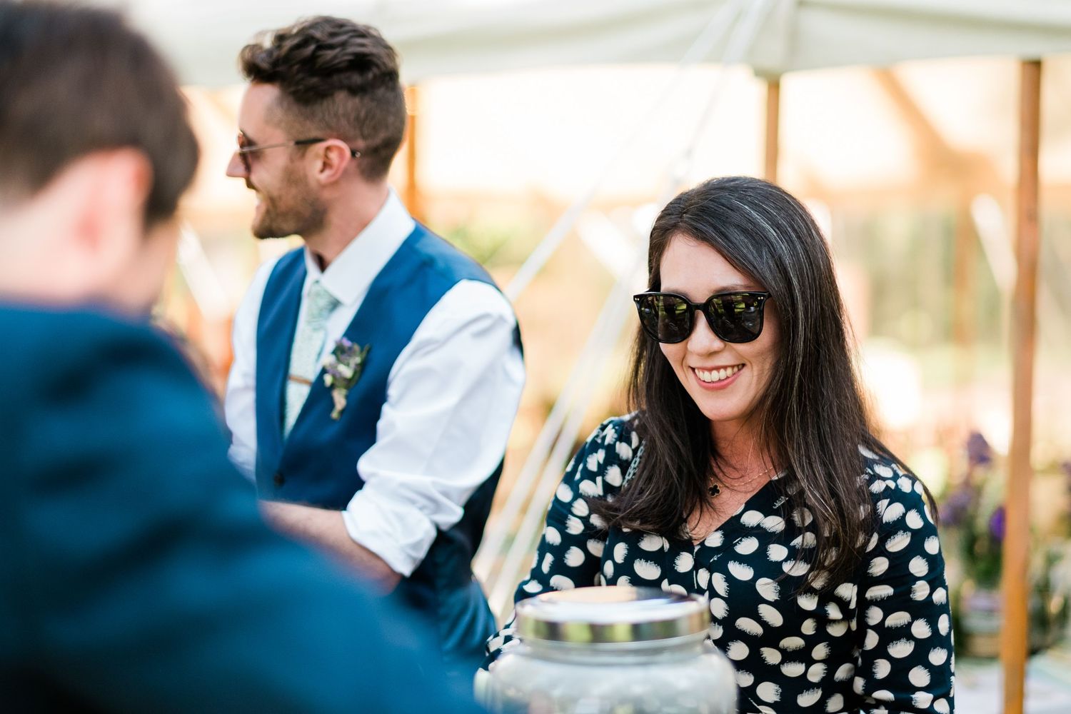 Wedding guests mingling under a white tent during an outdoor reception.