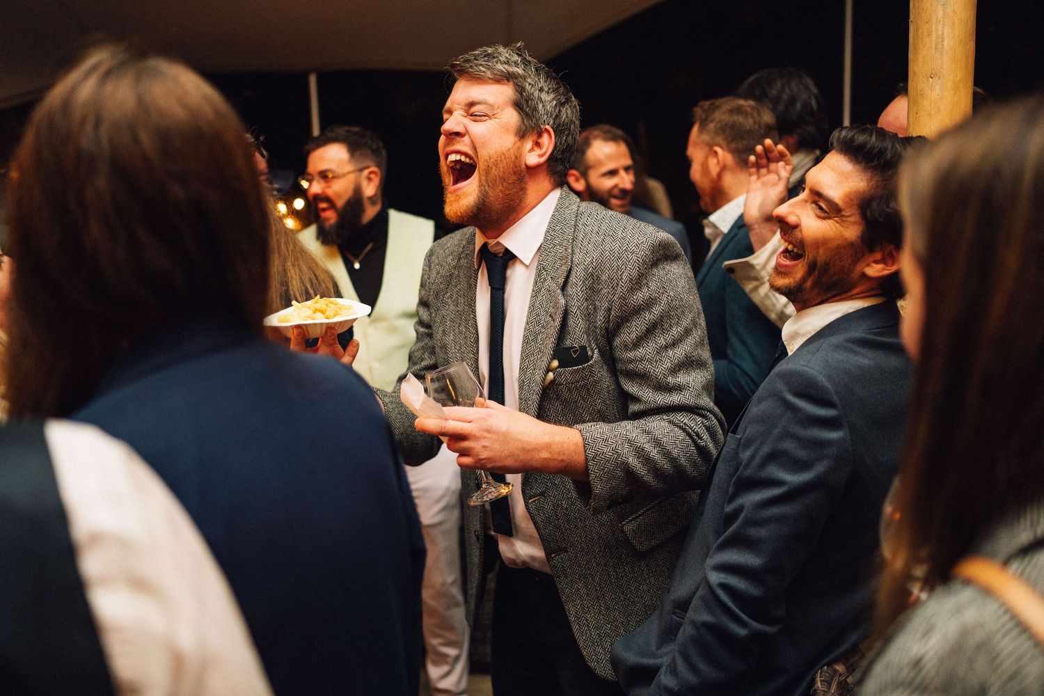 A group of guests sharing laughter and animated conversation during a social gathering indoors.