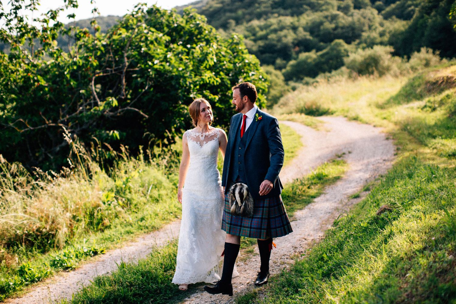 Couple walking along countryside path surrounded by lush green hills.