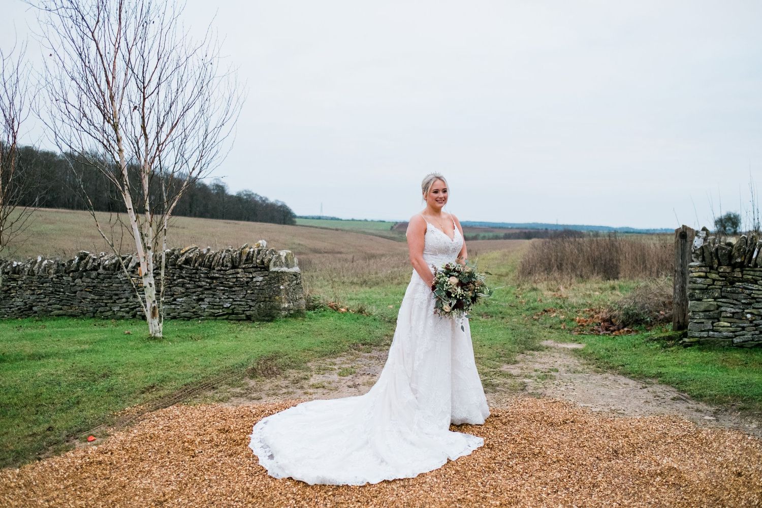 Wedding couple poses in a series of outdoor shots along a gravel path with stone walls and green fields.