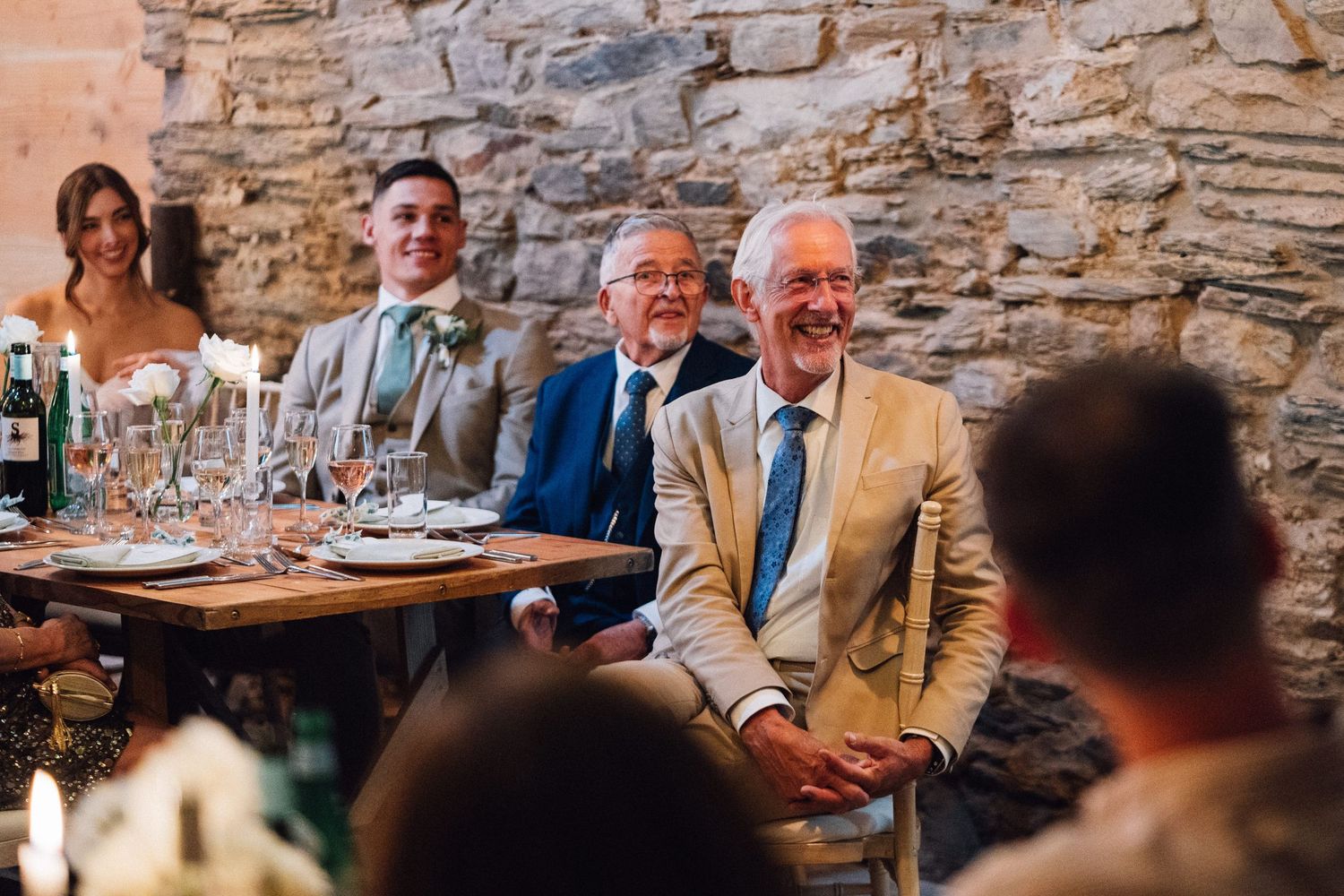 Wedding guests enjoy conversation and laughter at rustic stone-walled reception venue.
