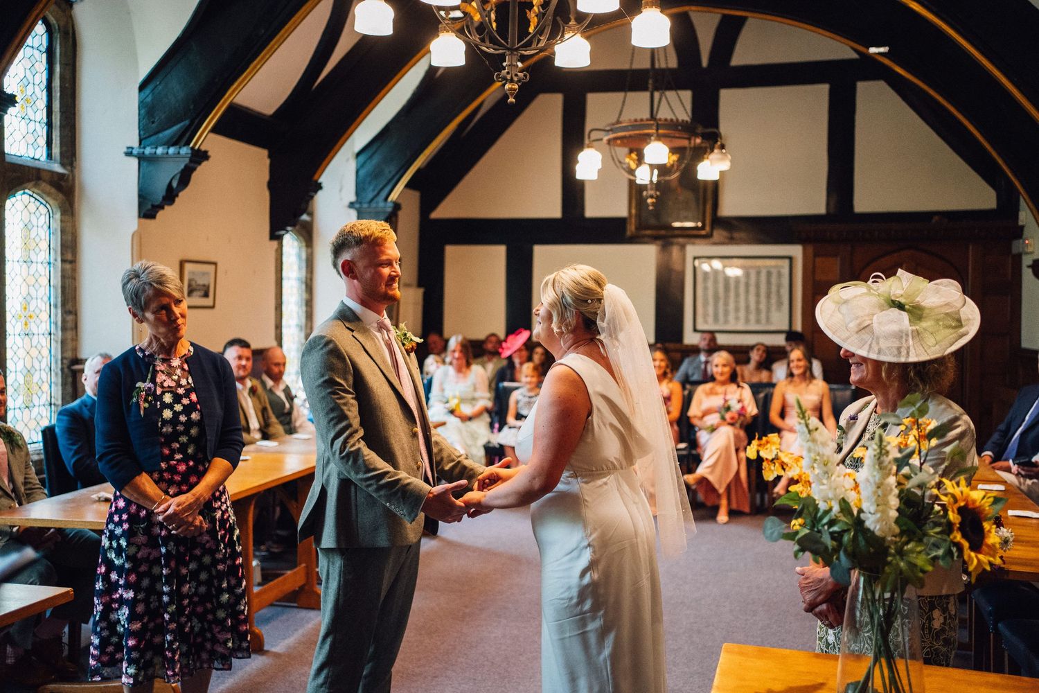 Wedding guests dance and celebrate together in a rustic venue with exposed wooden beams and warm lighting.