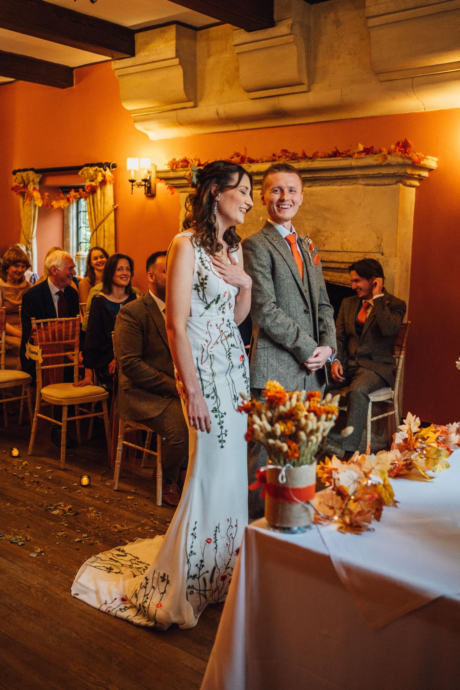 A wedding celebration in a warmly lit indoor venue with autumn-themed decorations and floral arrangements.