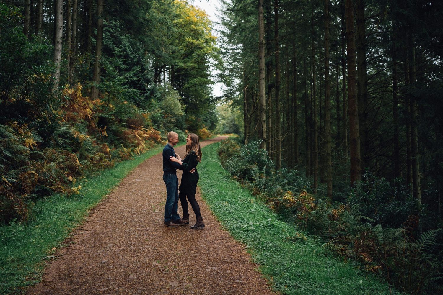 Couple walking along a scenic forest trail surrounded by tall evergreen trees.