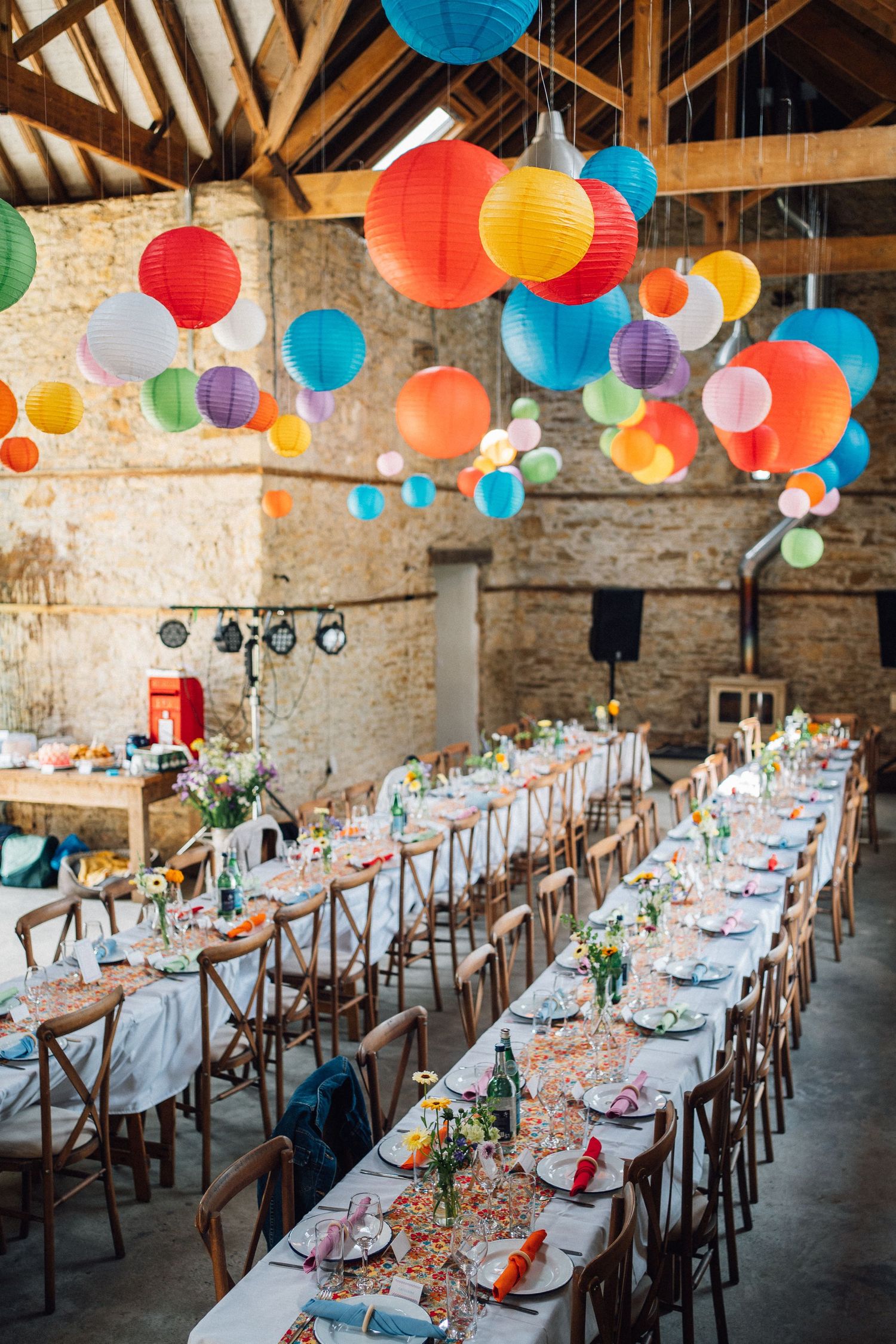 Colorful paper lanterns decorate a rustic barn wedding reception with long banquet tables.