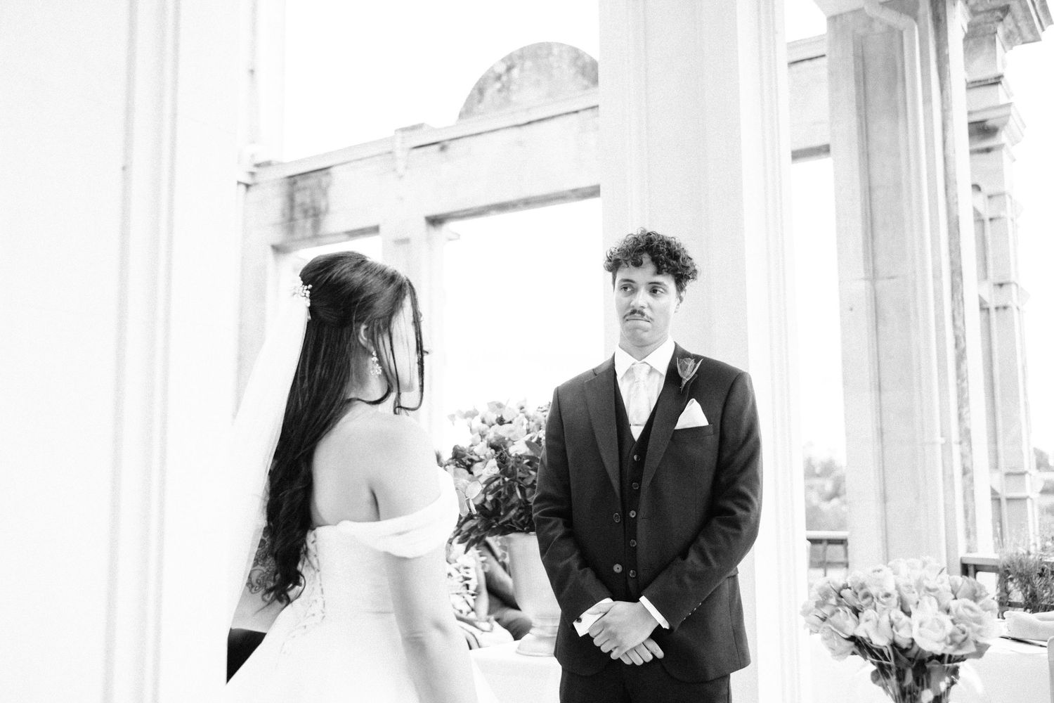 Black and white photo of a couple during their wedding ceremony under classical architecture.