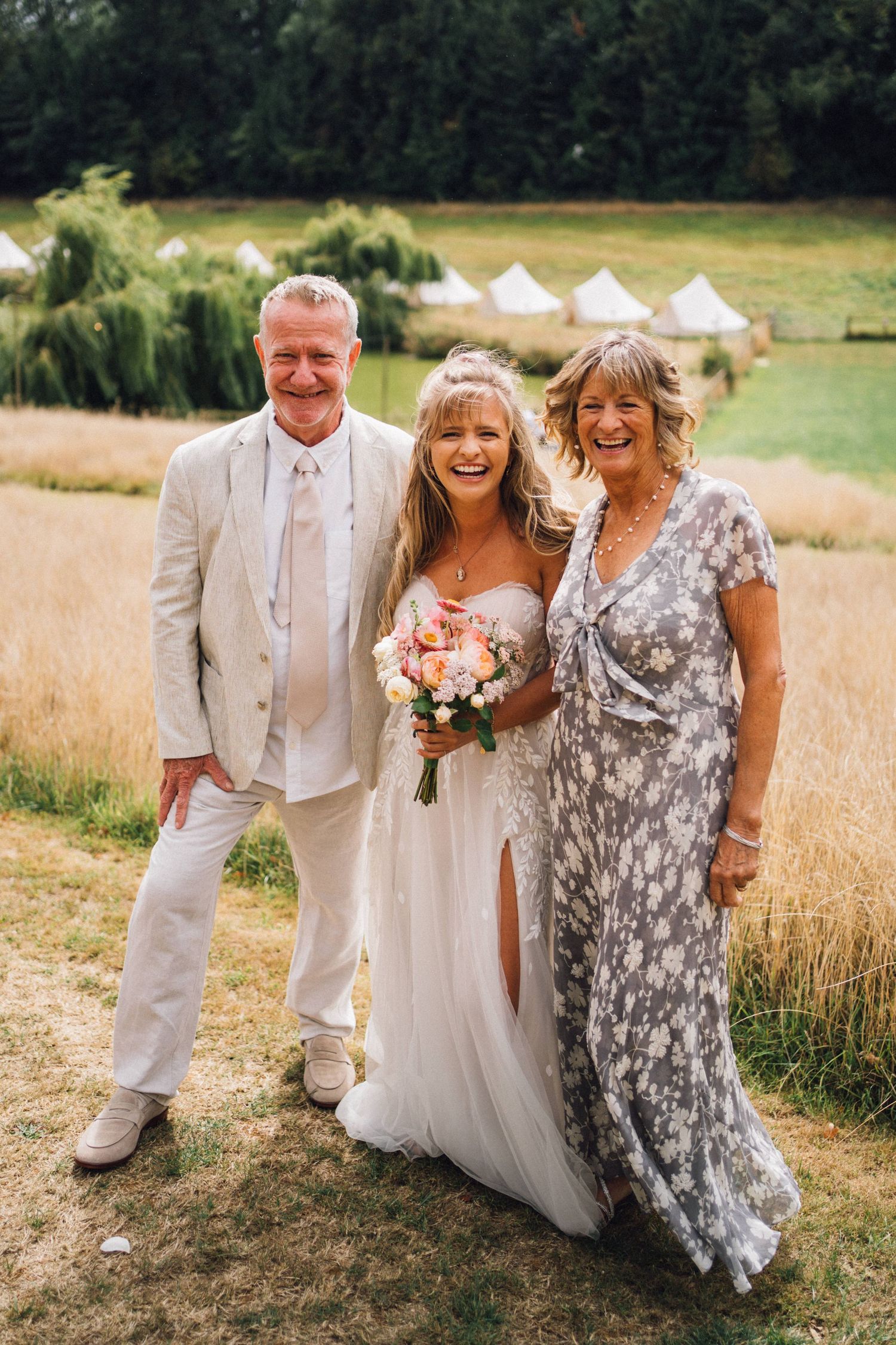 Wedding party poses together in a field with bell tents visible in the background.