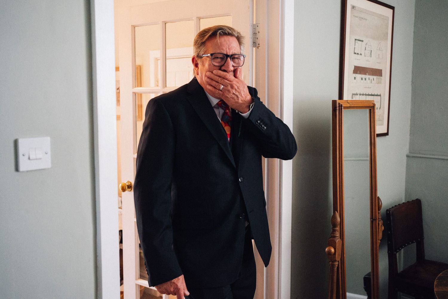 A person in formal attire stands in a doorway showing an emotional reaction.