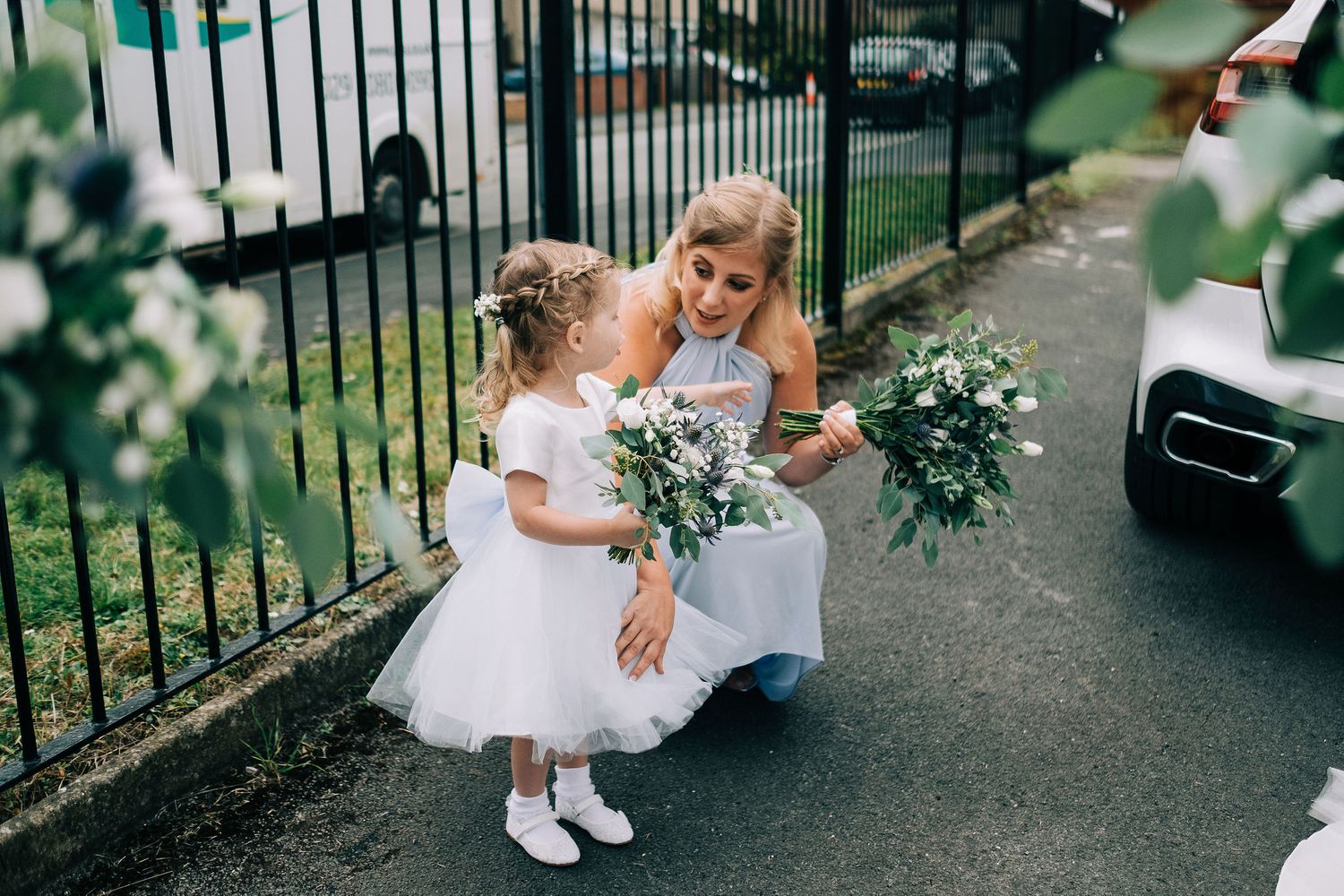 A tender moment between a bride and young flower girl holding bouquets on a pathway.