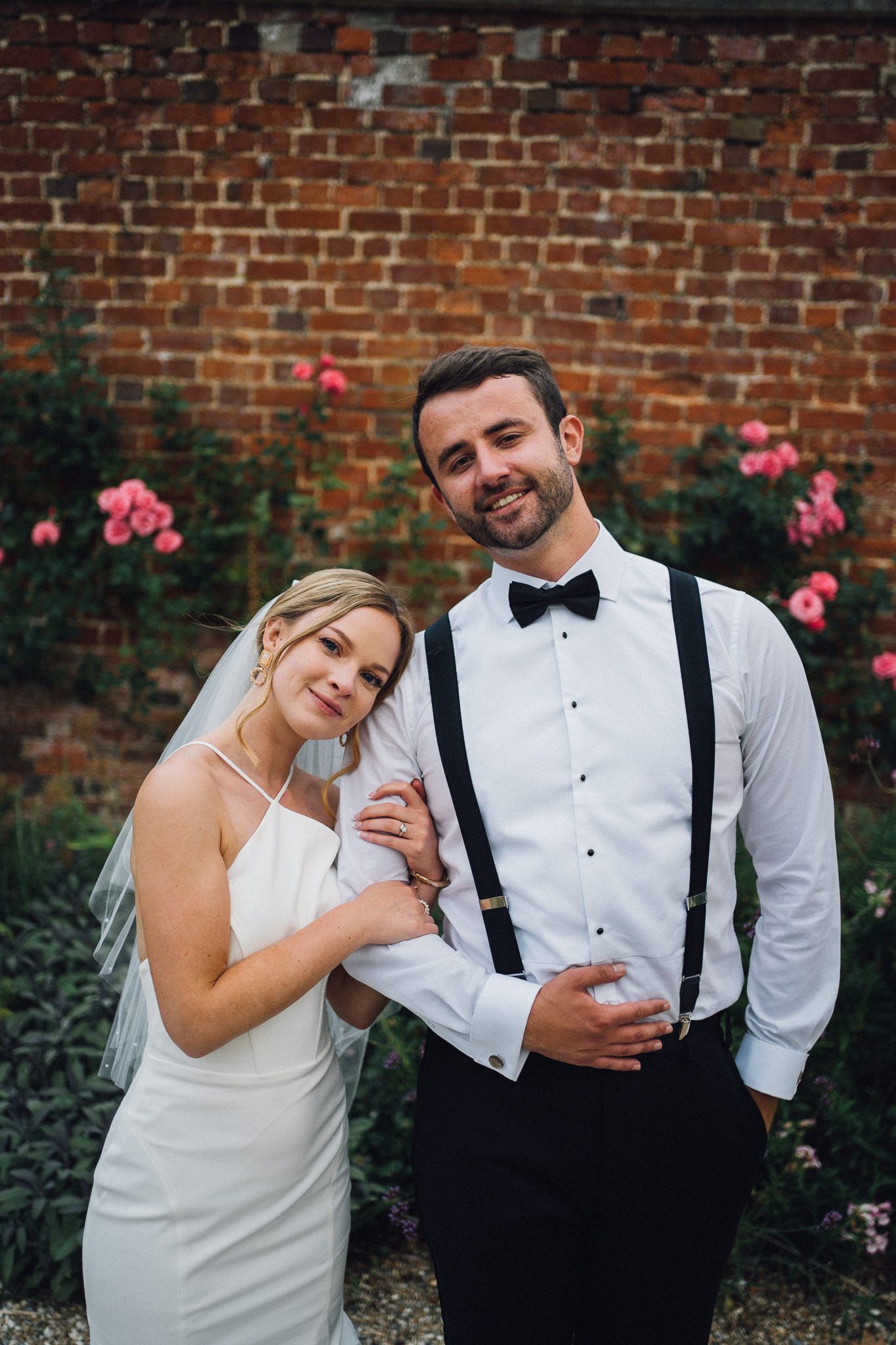Newlyweds share intimate moments against a backdrop of blooming pink flowers and brick walls.
