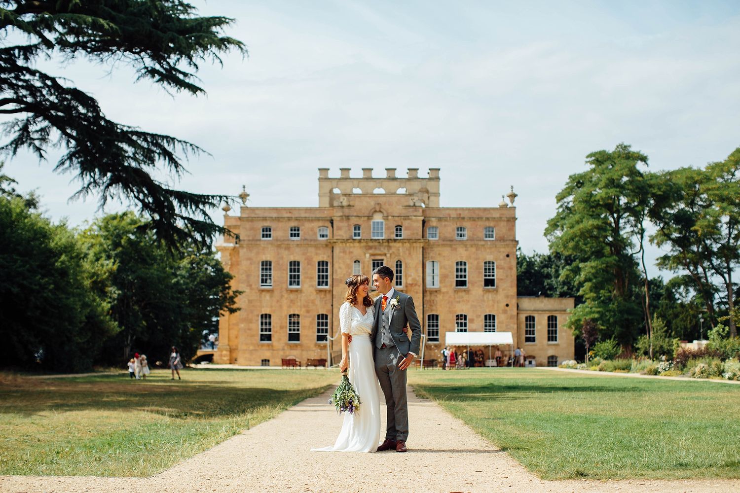 A wedding couple poses in front of a magnificent brick manor house on manicured grounds.