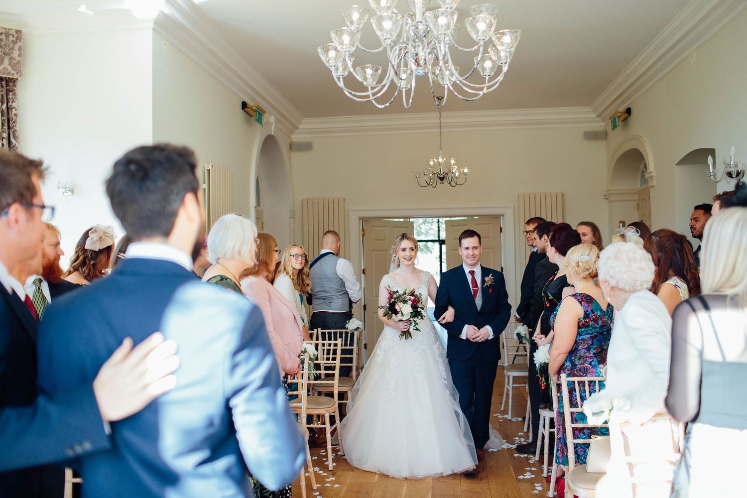Elegant wedding venue interior with crystal chandelier and gathered guests.