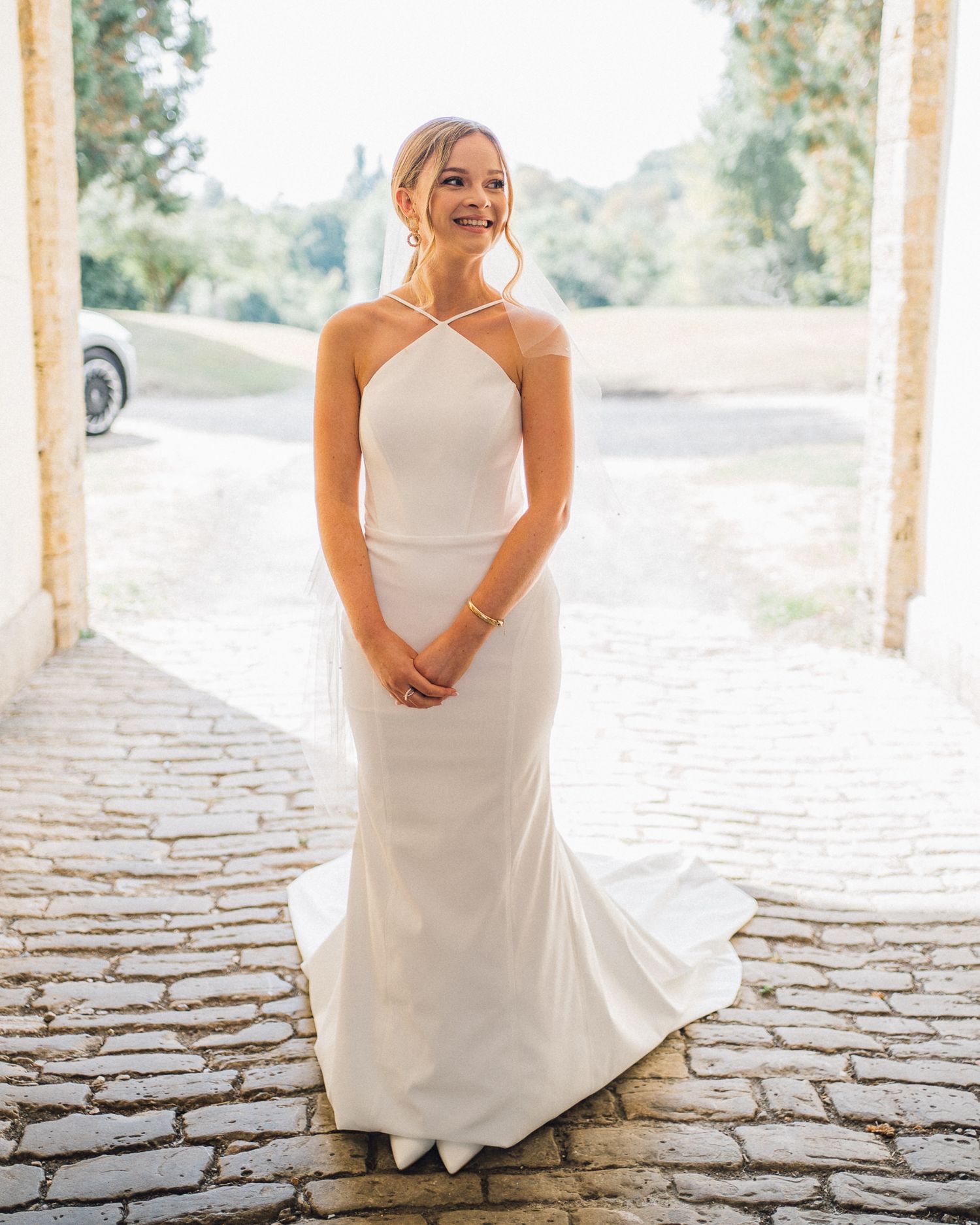 A elegant bride poses in a halter-neck wedding dress on a cobblestone pathway.