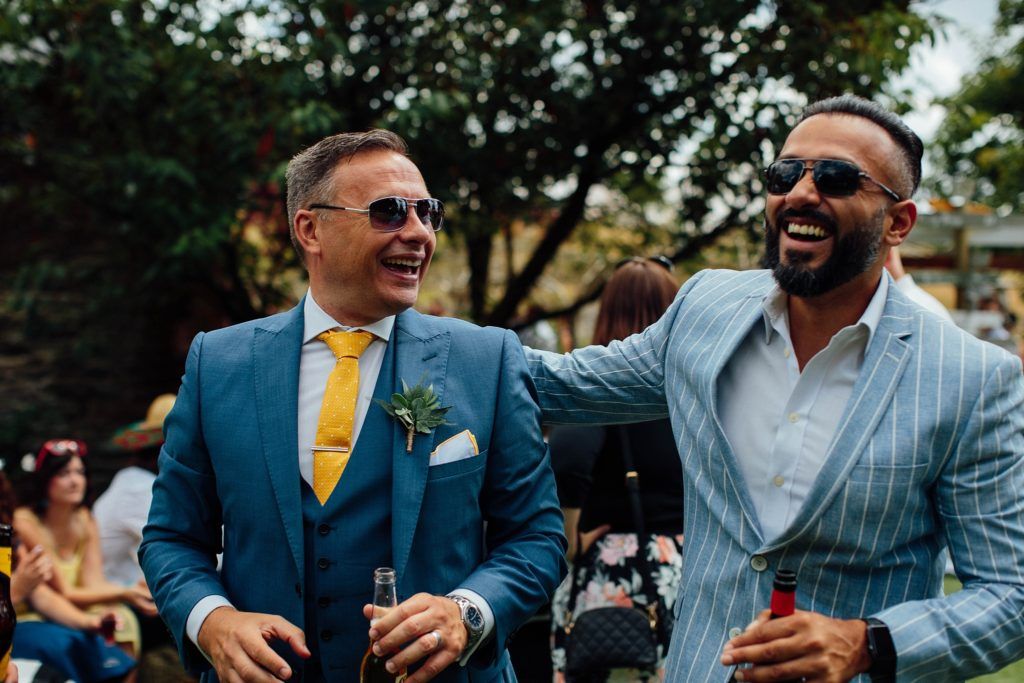 Wedding party members in blue suits and yellow ties celebrating outdoors.