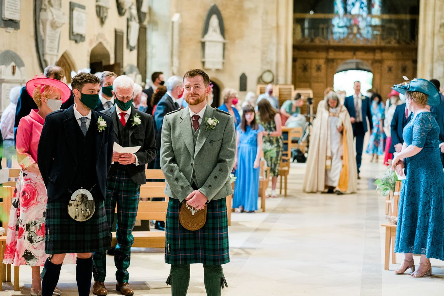 Wedding guests in kilts and formal attire gathered inside historic stone church.
