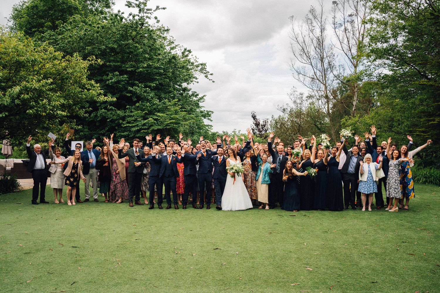 Panoramic shot of wedding guests gathered on a lush green lawn.