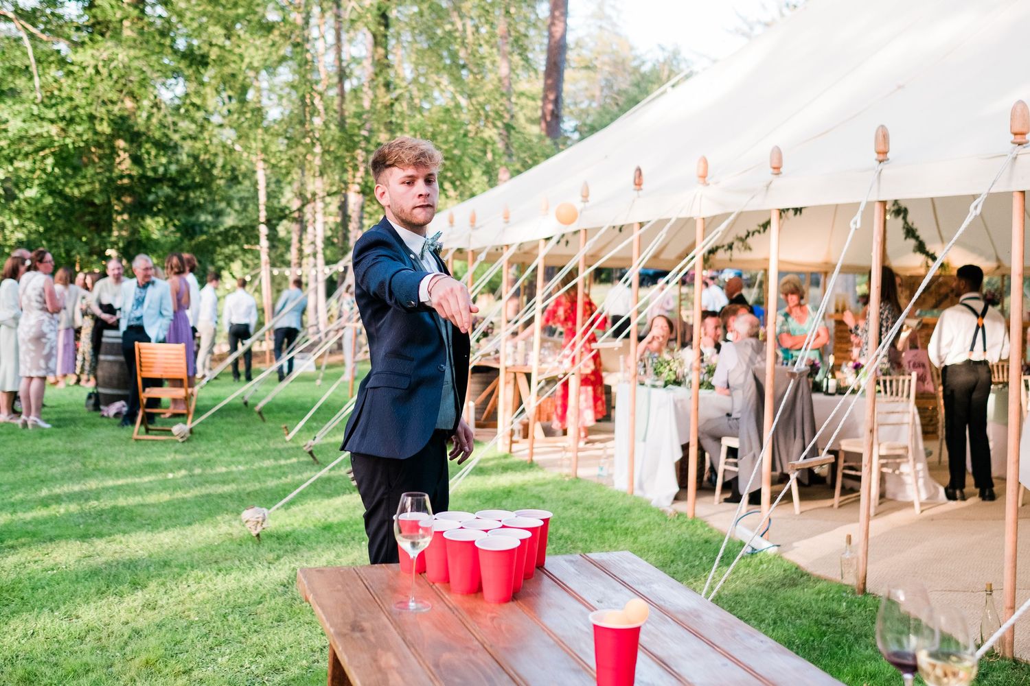 Wedding guests mingle under an elegant outdoor tent reception setup with string lights and rustic decor.
