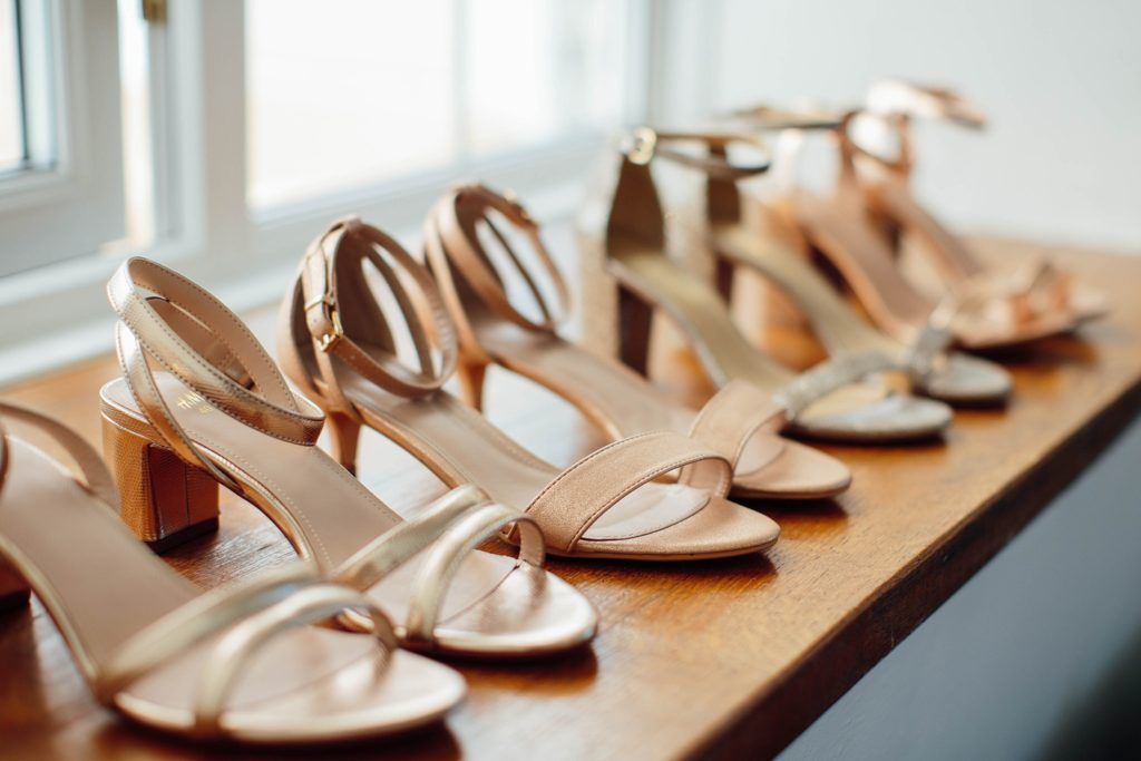 Row of elegant champagne-colored wedding shoes lined up on wooden surface.