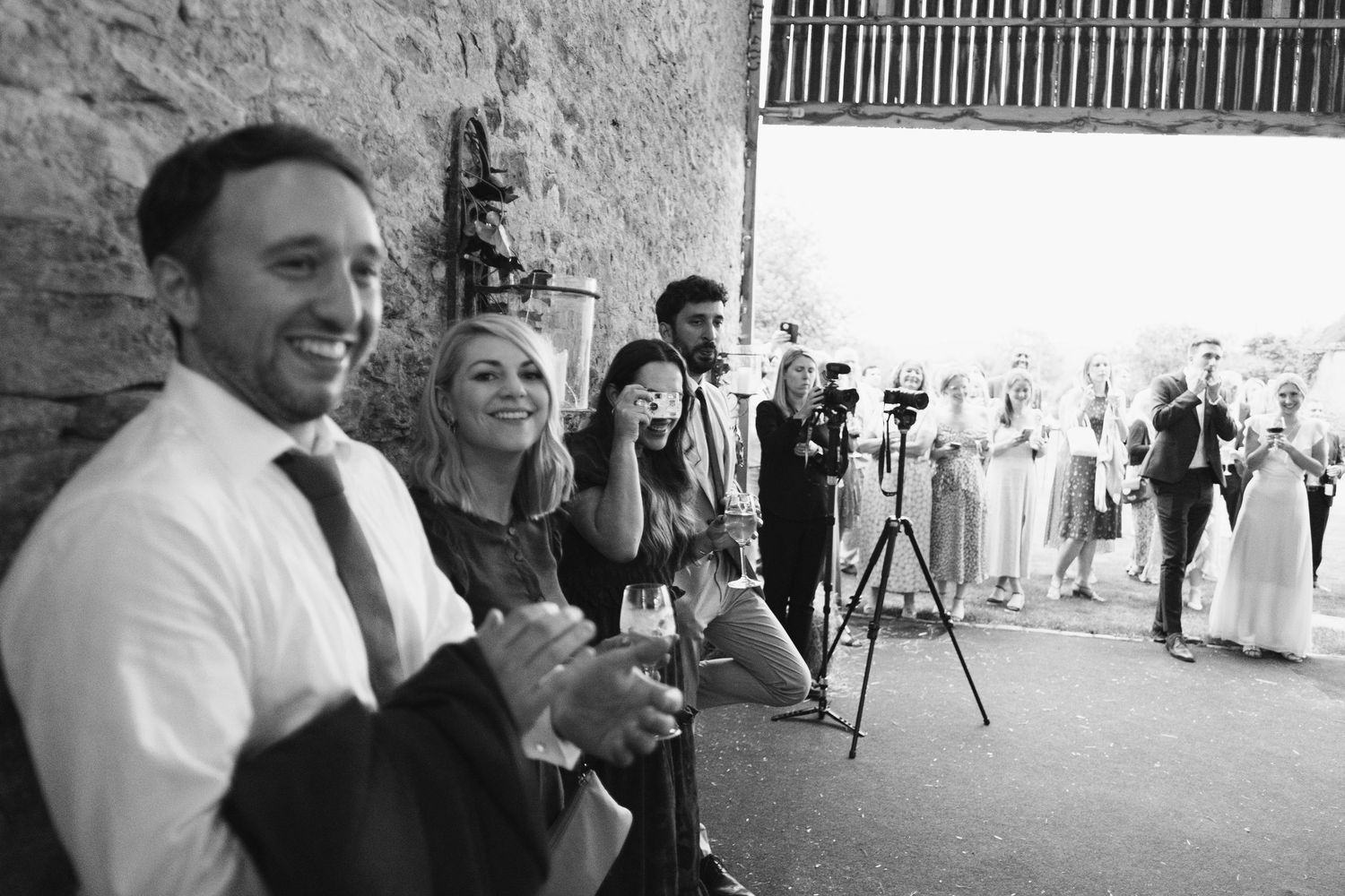 Black and white photo of wedding guests mingling in a rustic barn setting.