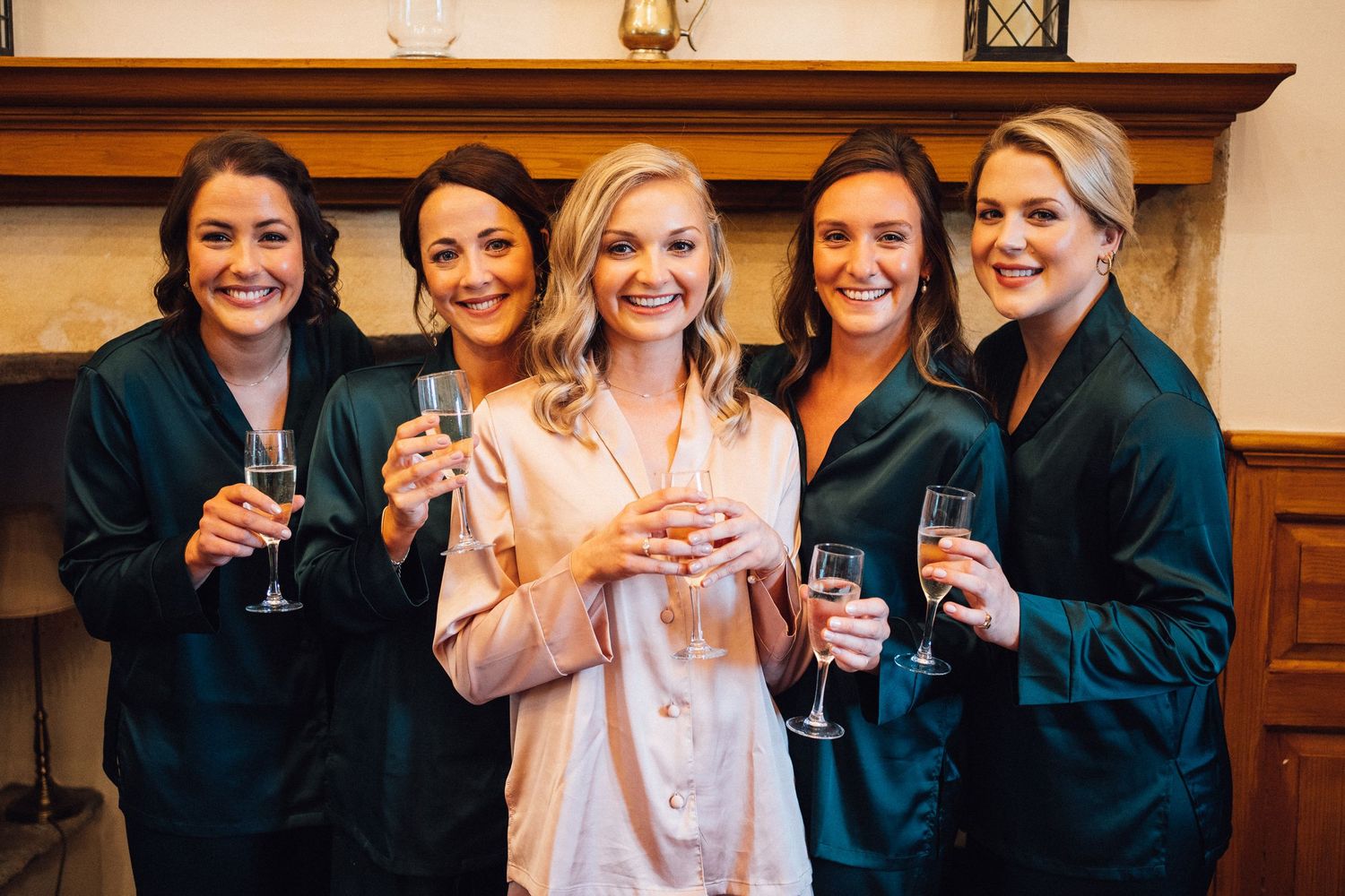 A group in matching dark robes and one in pink pajamas hold up champagne glasses while smiling together.